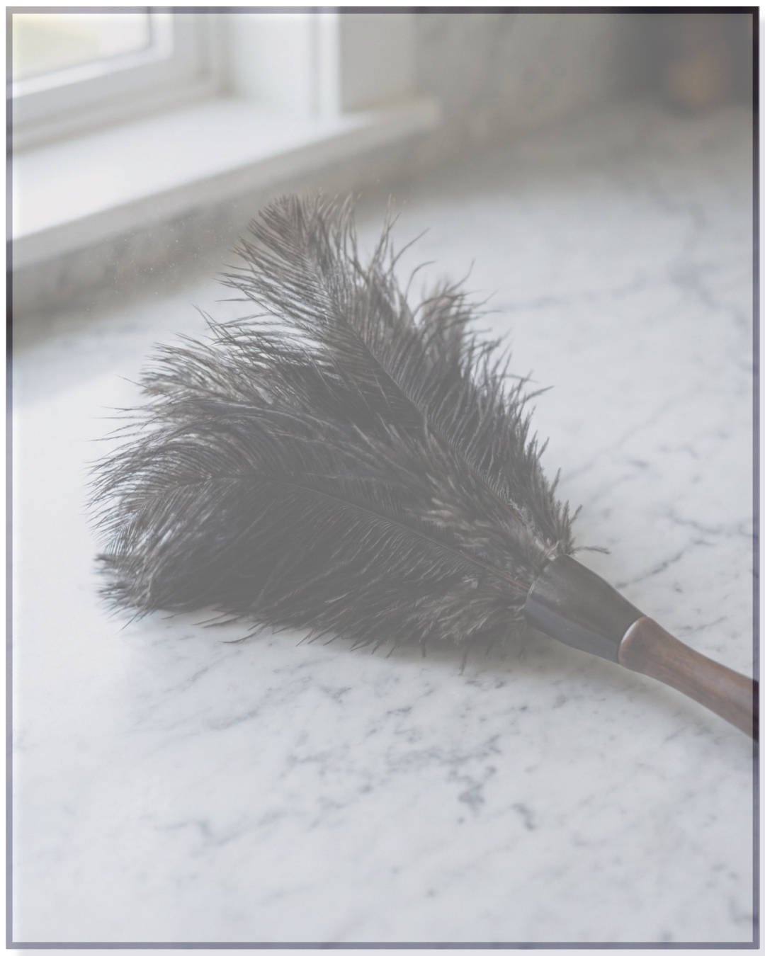 A feather duster with black feathers and a wooden handle resting on a white marble surface near a window.