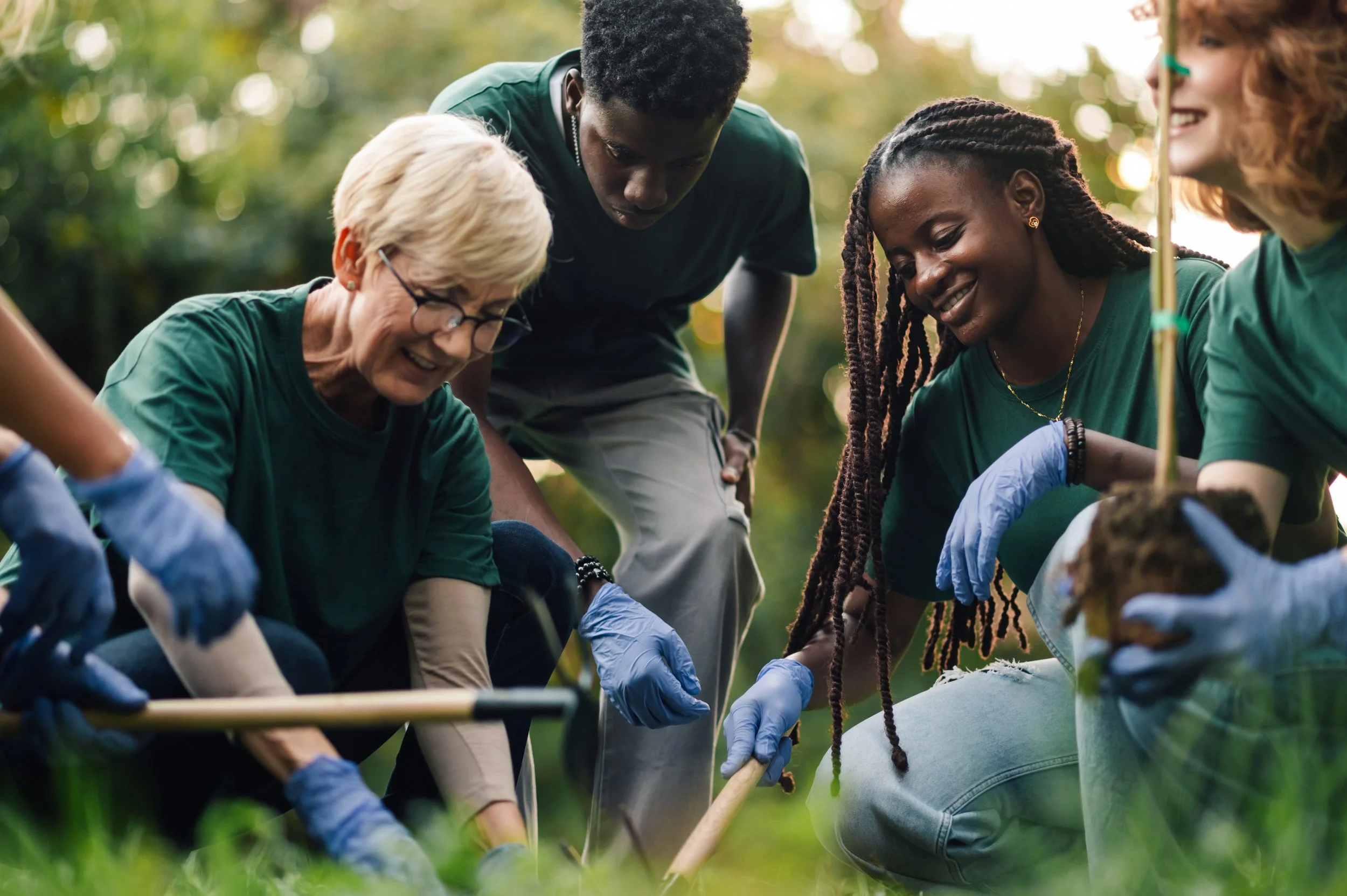 Group of diverse volunteers working together on a community gardening project outdoors, wearing gloves and using tools.