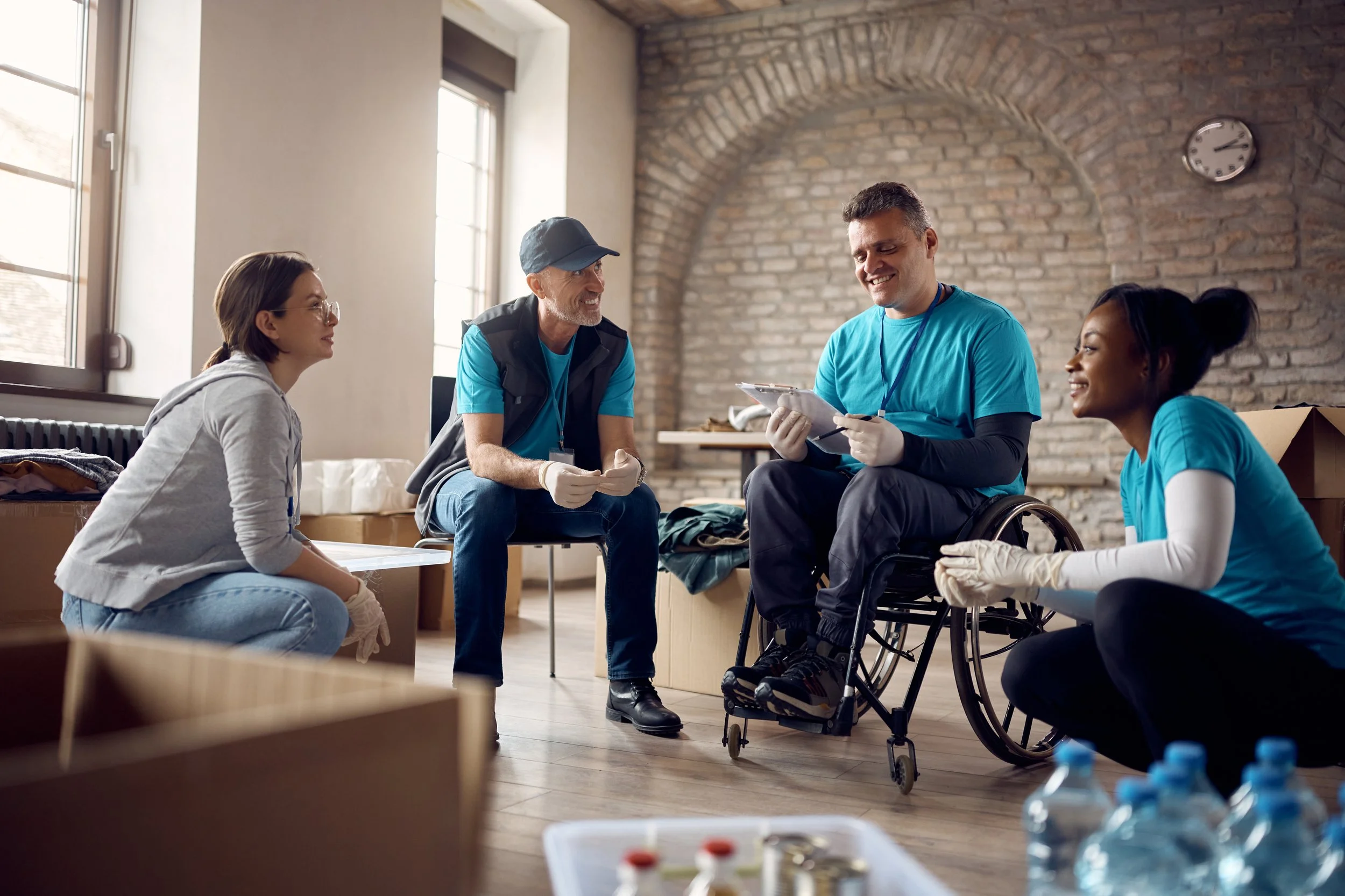 Group of diverse volunteers helping and interacting with a person in a wheelchair, in a community center or similar indoor space.