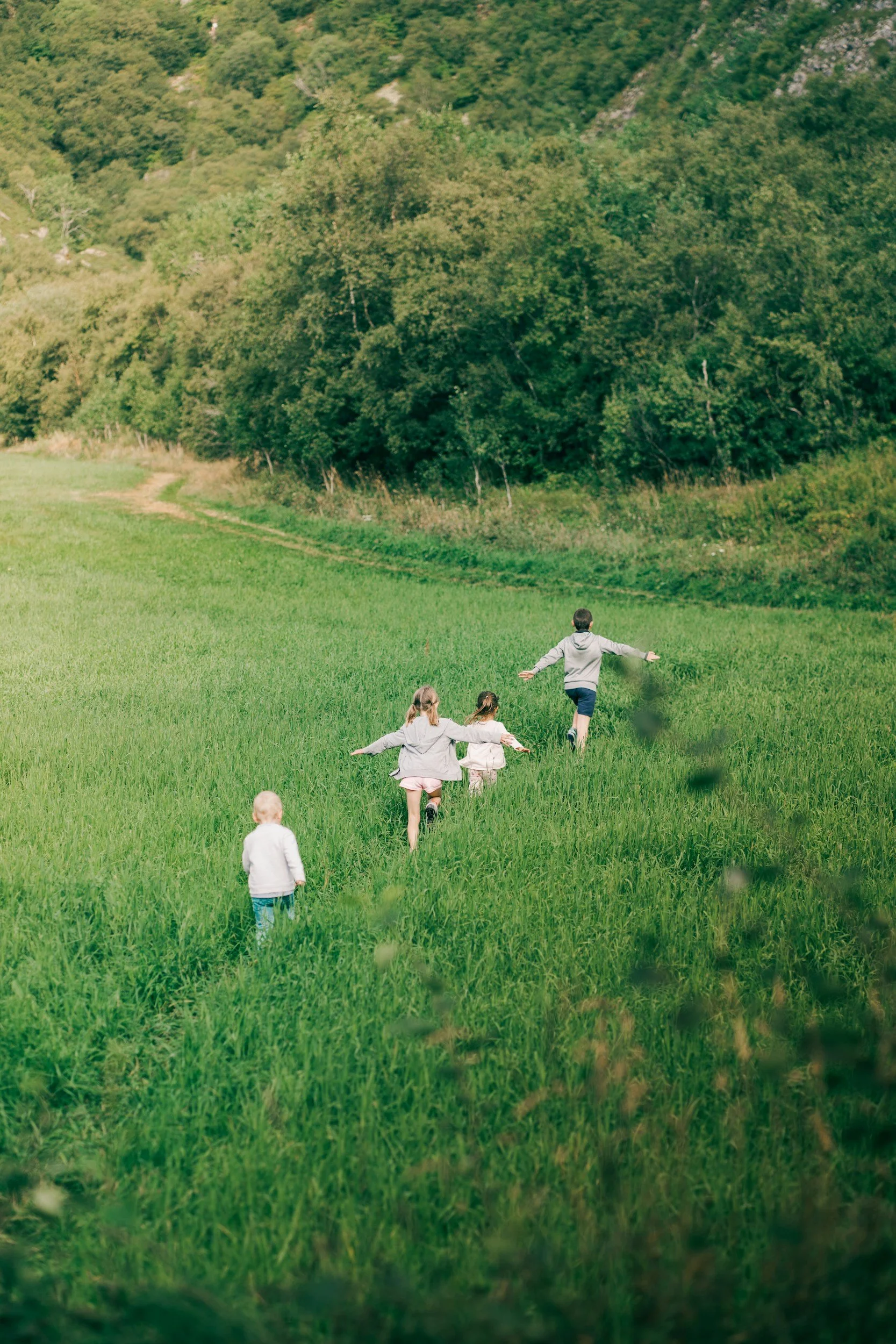 A group of children running through a grassy field with a backdrop of trees and hills, with one boy in the lead and others following behind. Wildflower Neuro Scarborough North Yorkshire