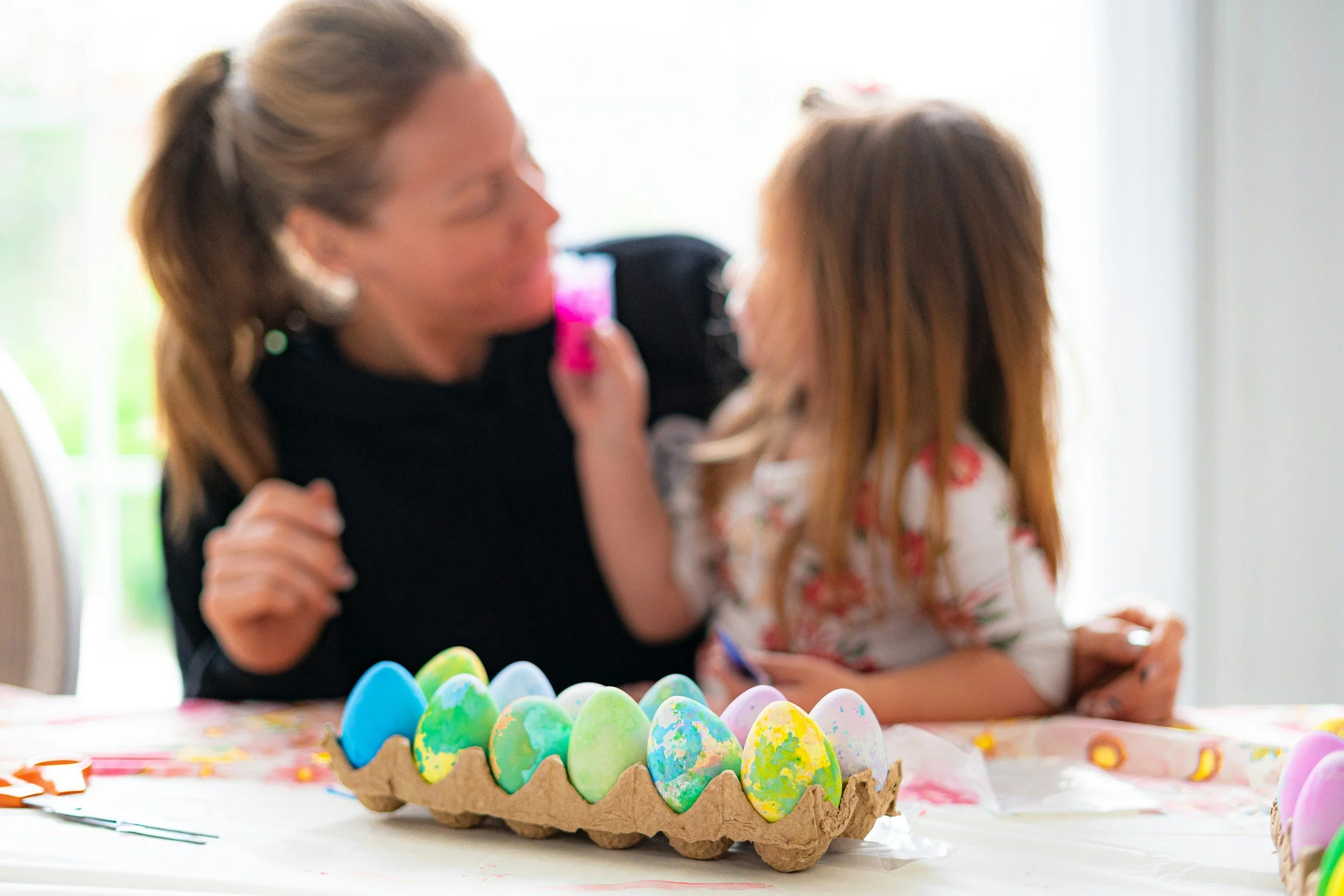 Child and adult decorating colorful Easter eggs in a paper egg carton on a table. Wildflower Neuro Scarborough North Yorkshire