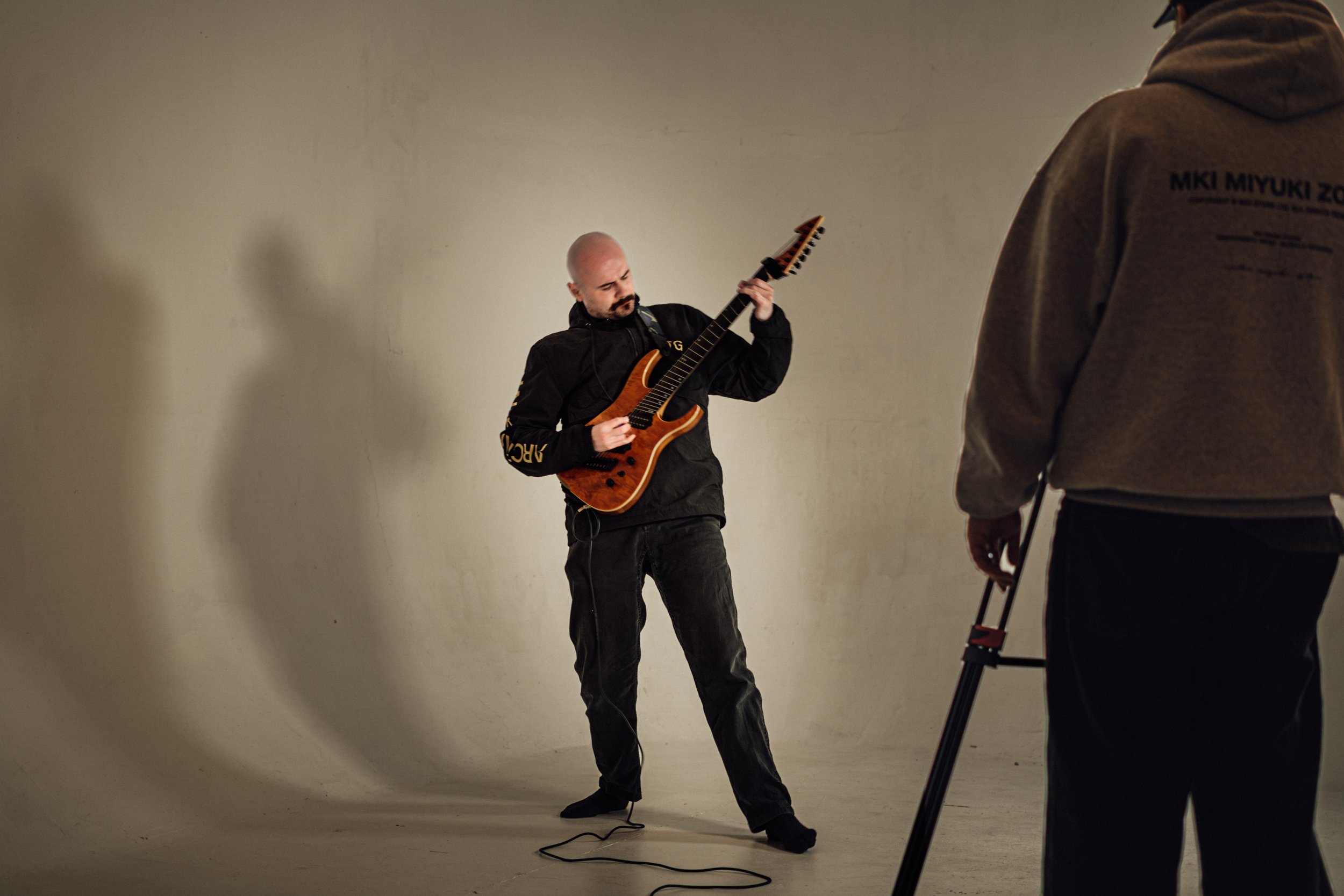 A man playing an electric guitar during a photo shoot in a studio with a plain wall background.