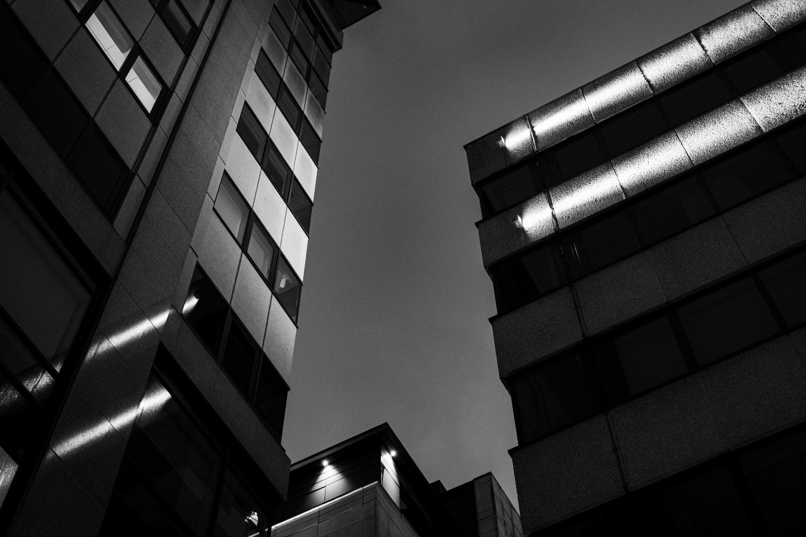 Low-angle view of modern multi-story buildings at night, with illuminated exterior lights and dark sky in the background.