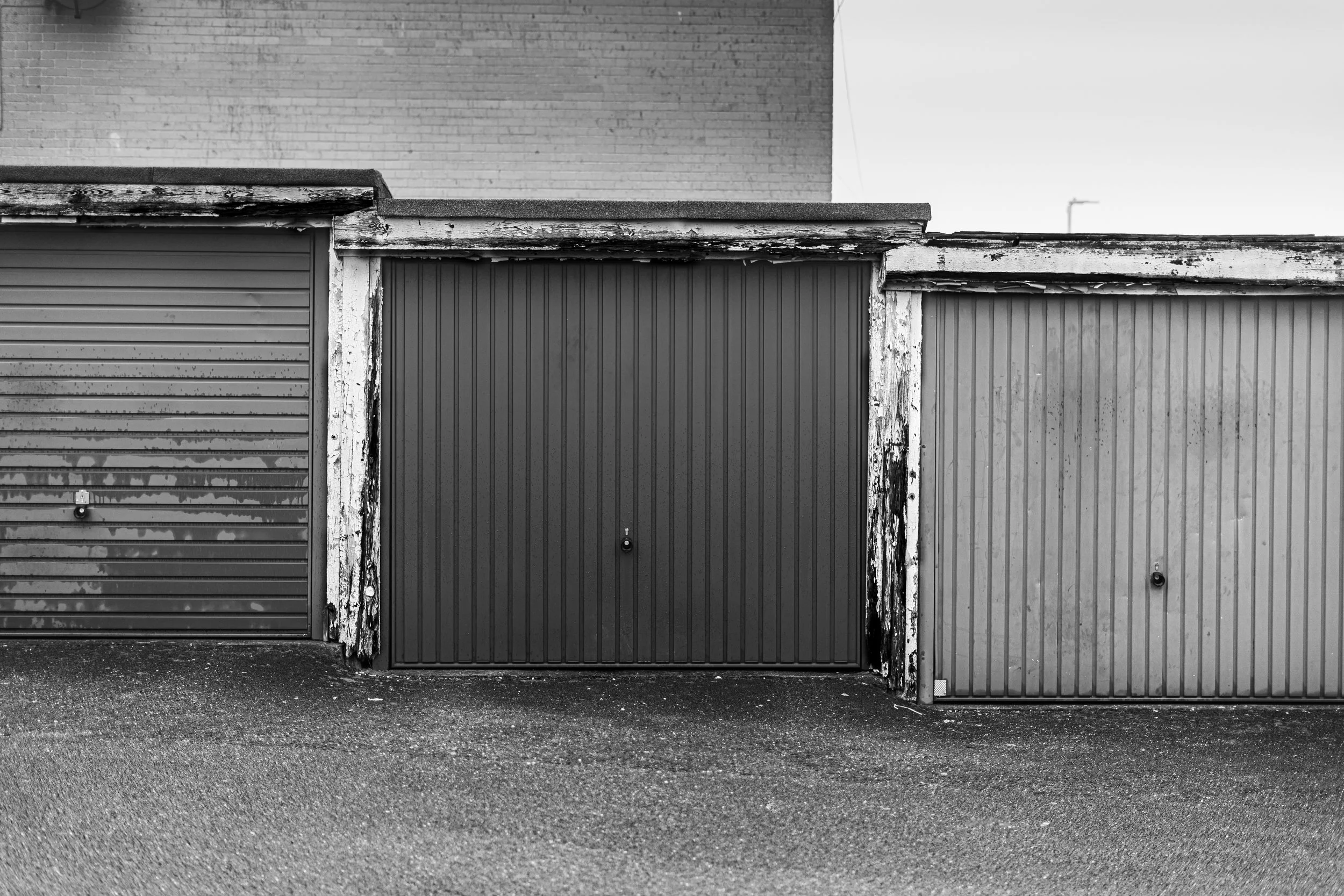 Three garage doors with different textures and colors, one rusted and peeling, the other two in better condition, under a brick building.