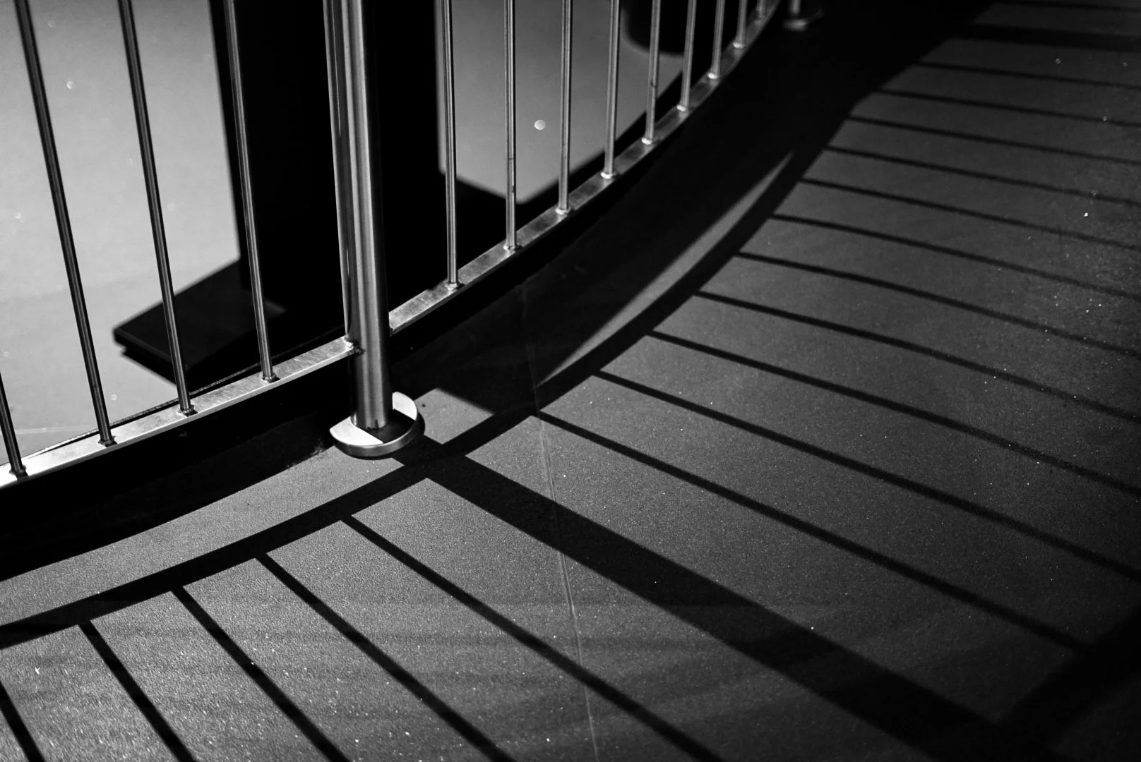 Black and white photo of a metal railing casting shadows on the ground.