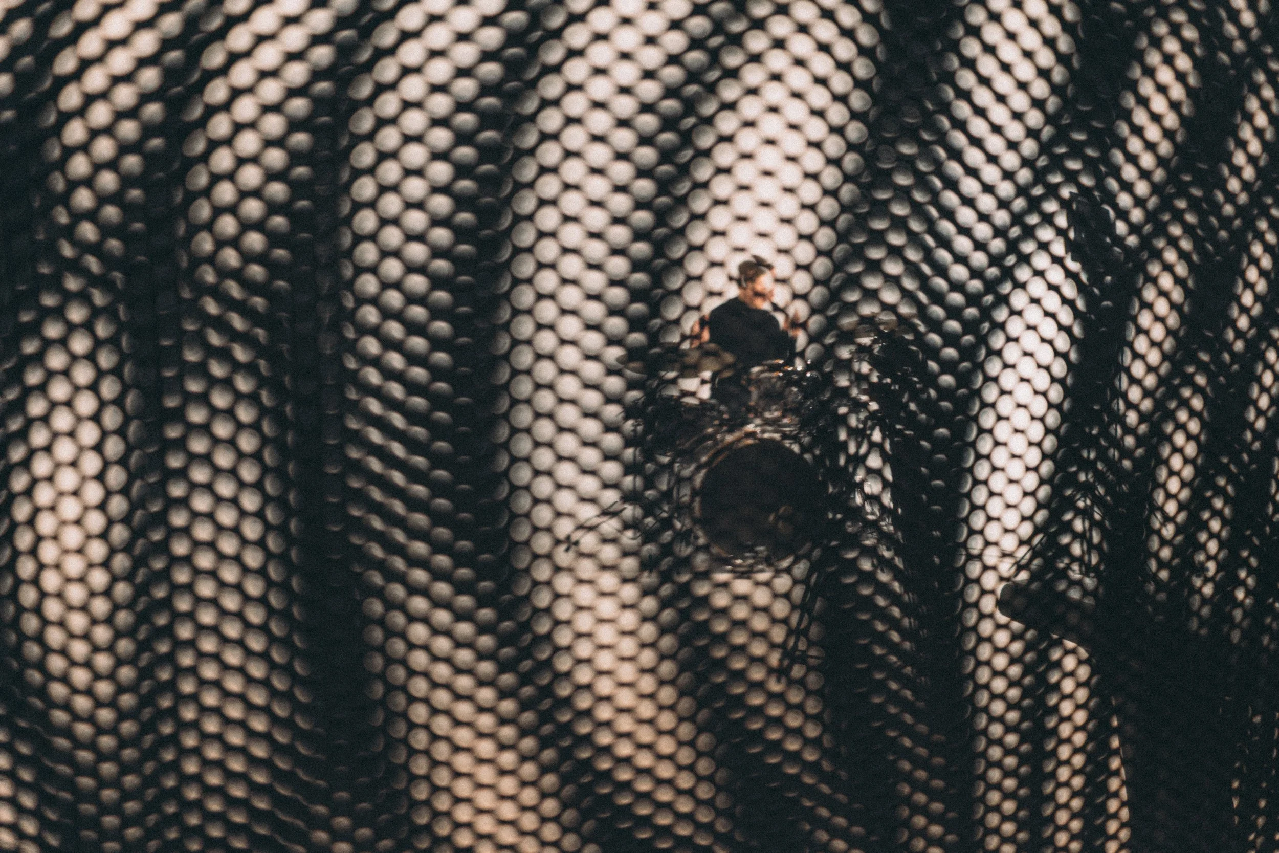 A close-up of a textured fabric with a person in sunglasses and dark clothing behind it.