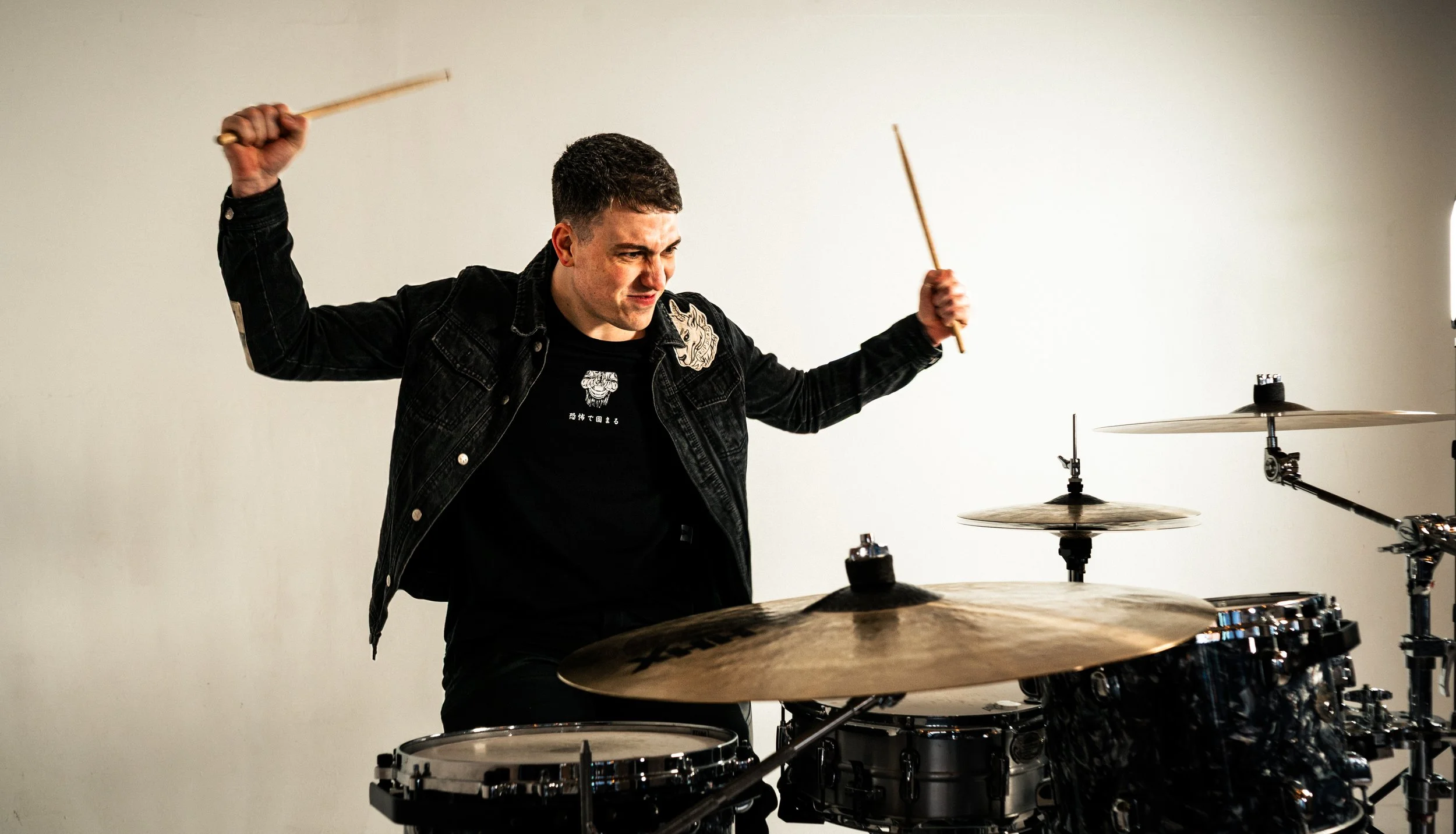 A man playing drums, holding drumsticks, with a focused expression.