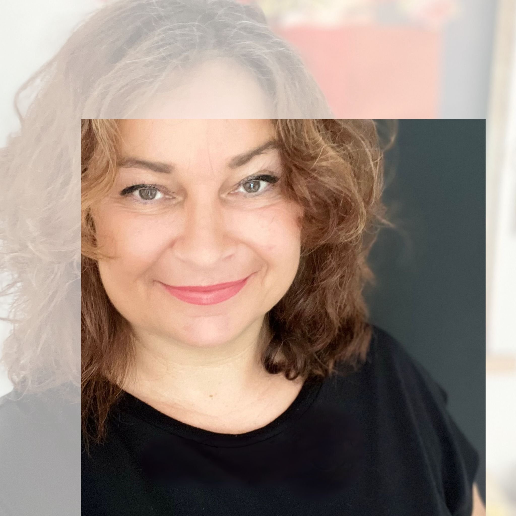 Portrait d'une femme souriante à cheveux bruns bouclés, portant un haut noir, dans un environnement intérieur.