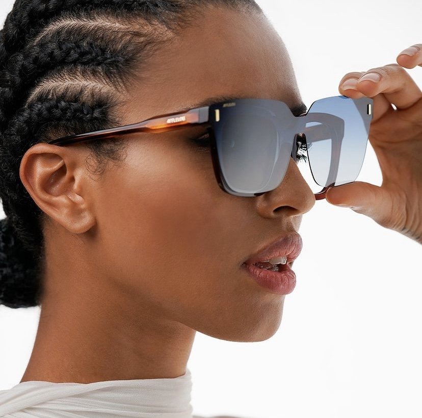 Une femme portant des lunettes de soleil graphiques avec un cadre brun et des verres dégradés.