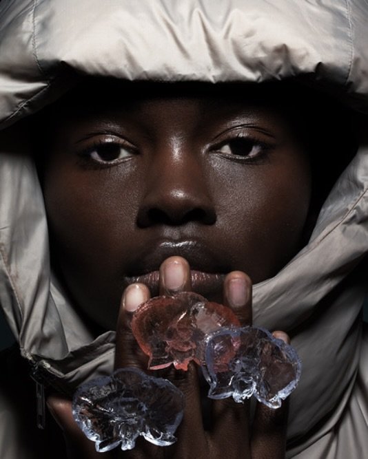 Personne noire portant une capuche grise, tenant du glaçon près des lèvres, regard fixe.