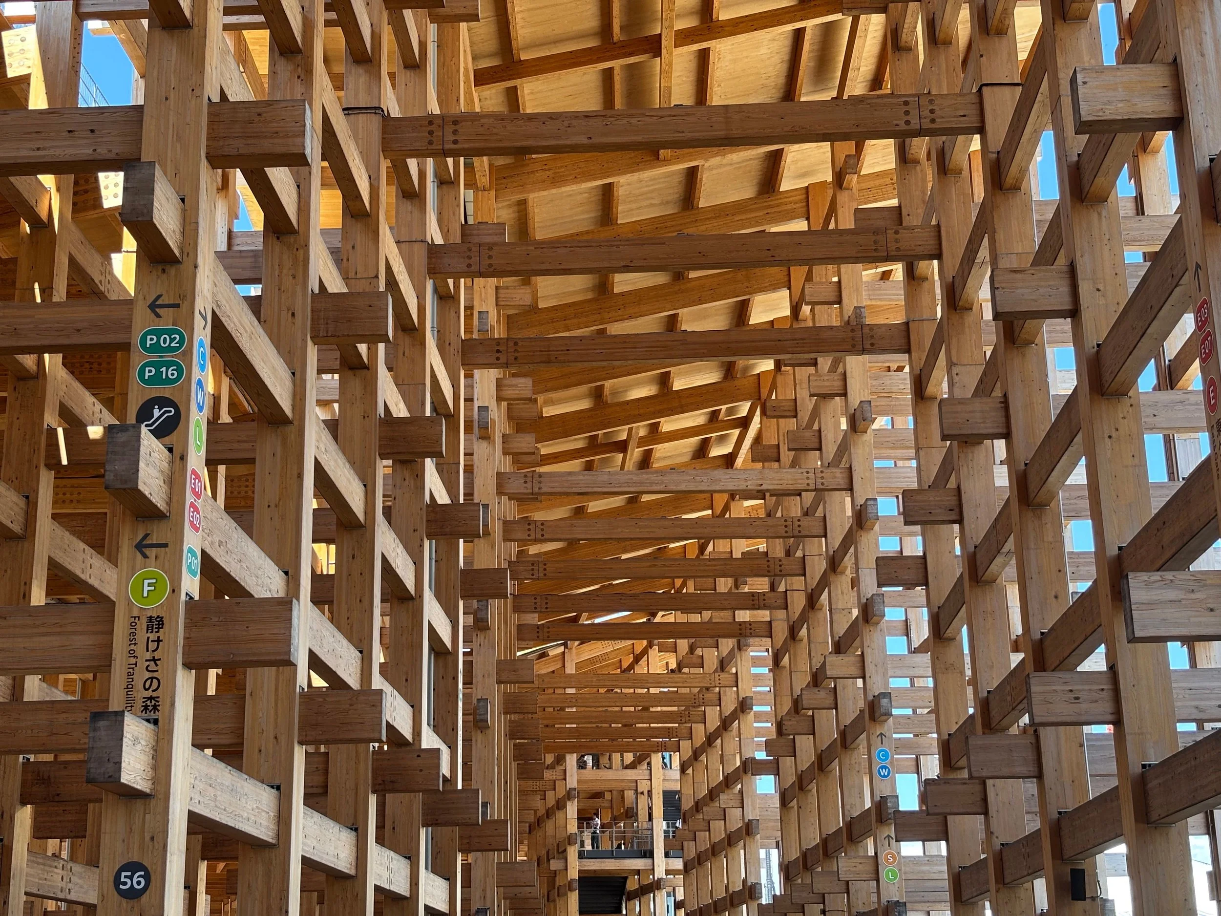 Innenansicht eines komplexen Holzbauten mit mehreren Stockwerken und durchgehenden offenen Bereichen, Sonnenlicht strömt durch große Fensterflächen.