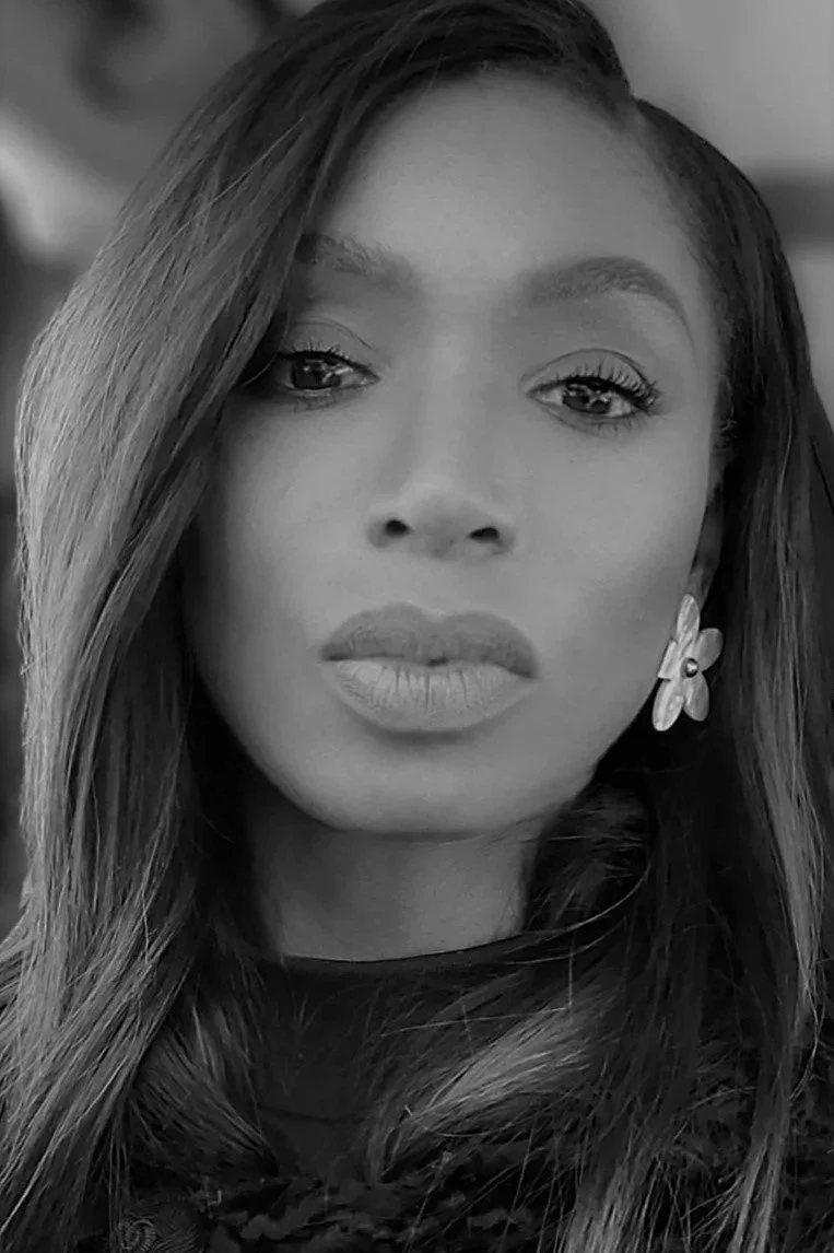 Close-up black-and-white portrait of a woman with long hair, wearing earrings, looking confidently at the camera.
