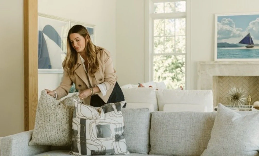 Lisa decorating with pillows on a gray sofa in a bright living room.