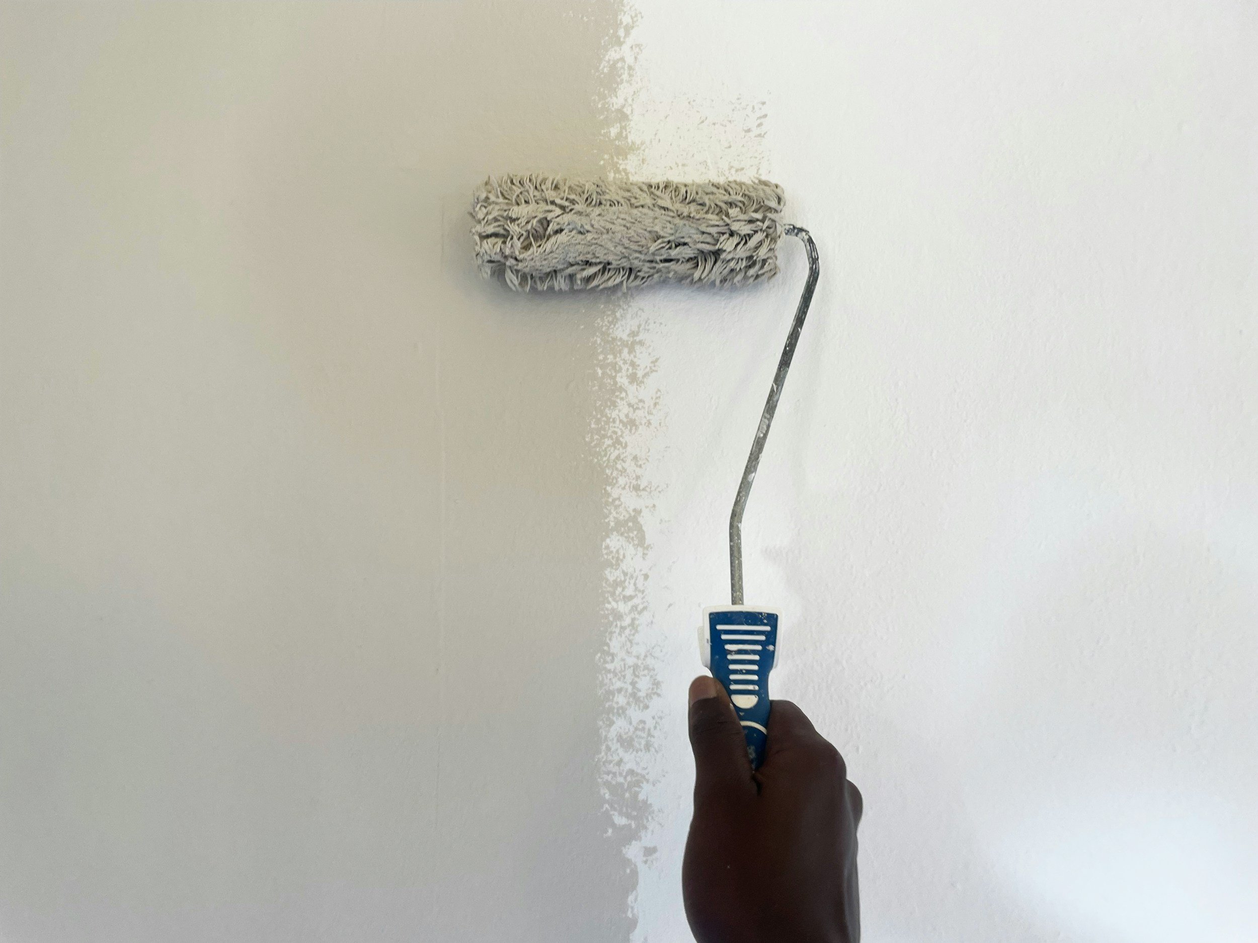 Person painting a wall with a paint roller, partially painted wall.