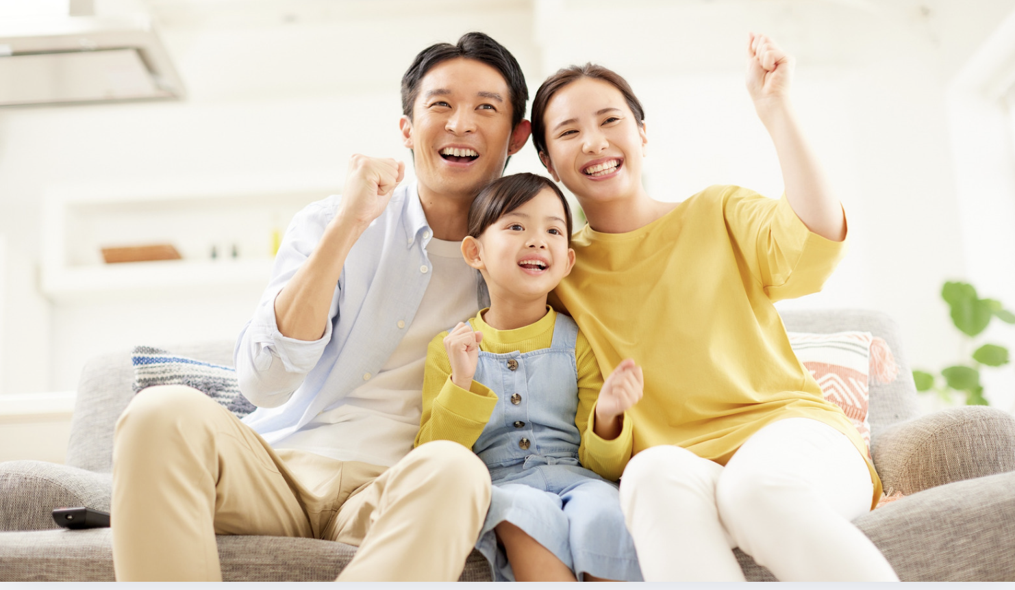Family of three sitting on a couch, smiling, and making fist gestures of triumph.