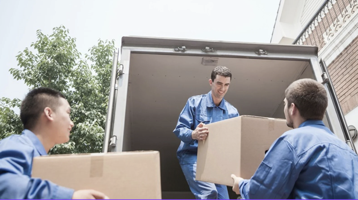 Three movers in blue uniforms unloading cardboard boxes from a moving truck.