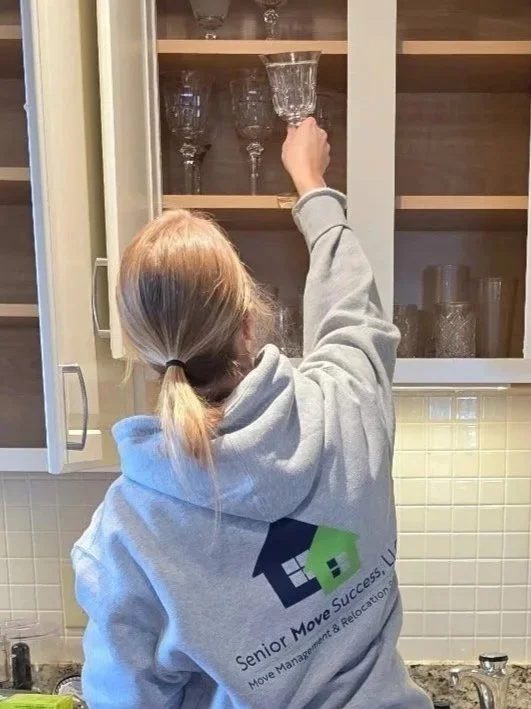 Living room with white sofa, decorative pillows, two side tables with lamps, framed abstract art on the wall, black coffee table with decorative items, potted plant, and two orange ottomans.