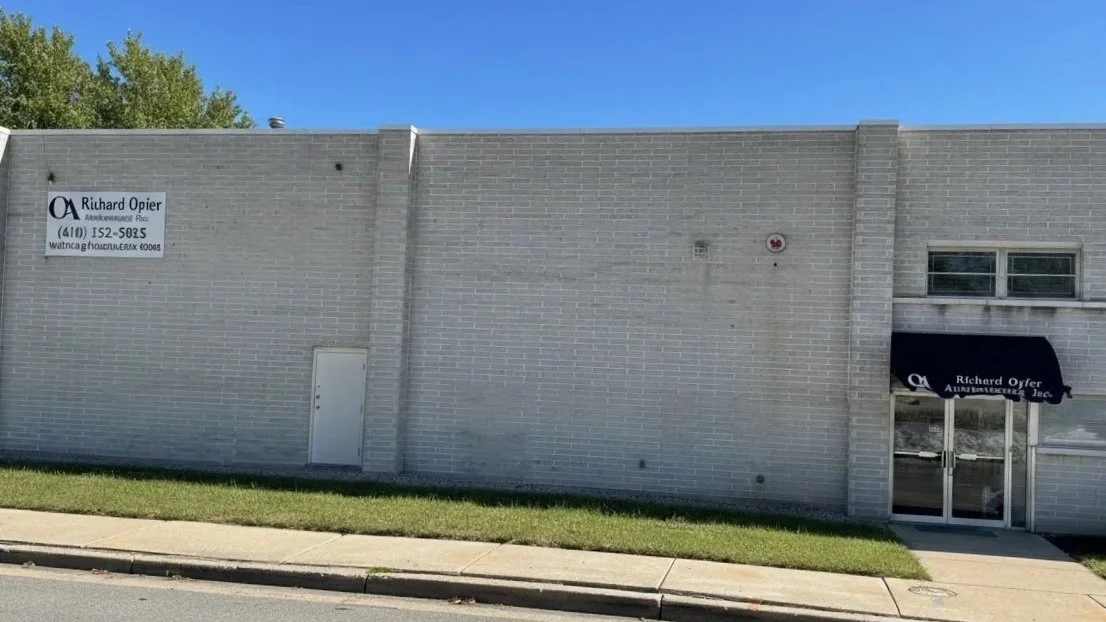 Front of a commercial building with a sign for Richard Opler, and an office entrance with a black awning sign.