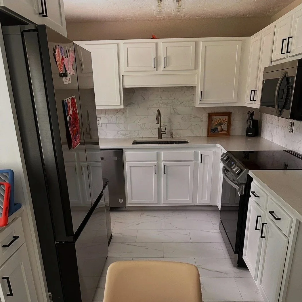 Modern kitchen with white cabinets, marble backsplash, stainless steel refrigerator, microwave, oven, and a single basin sink with a chrome faucet.