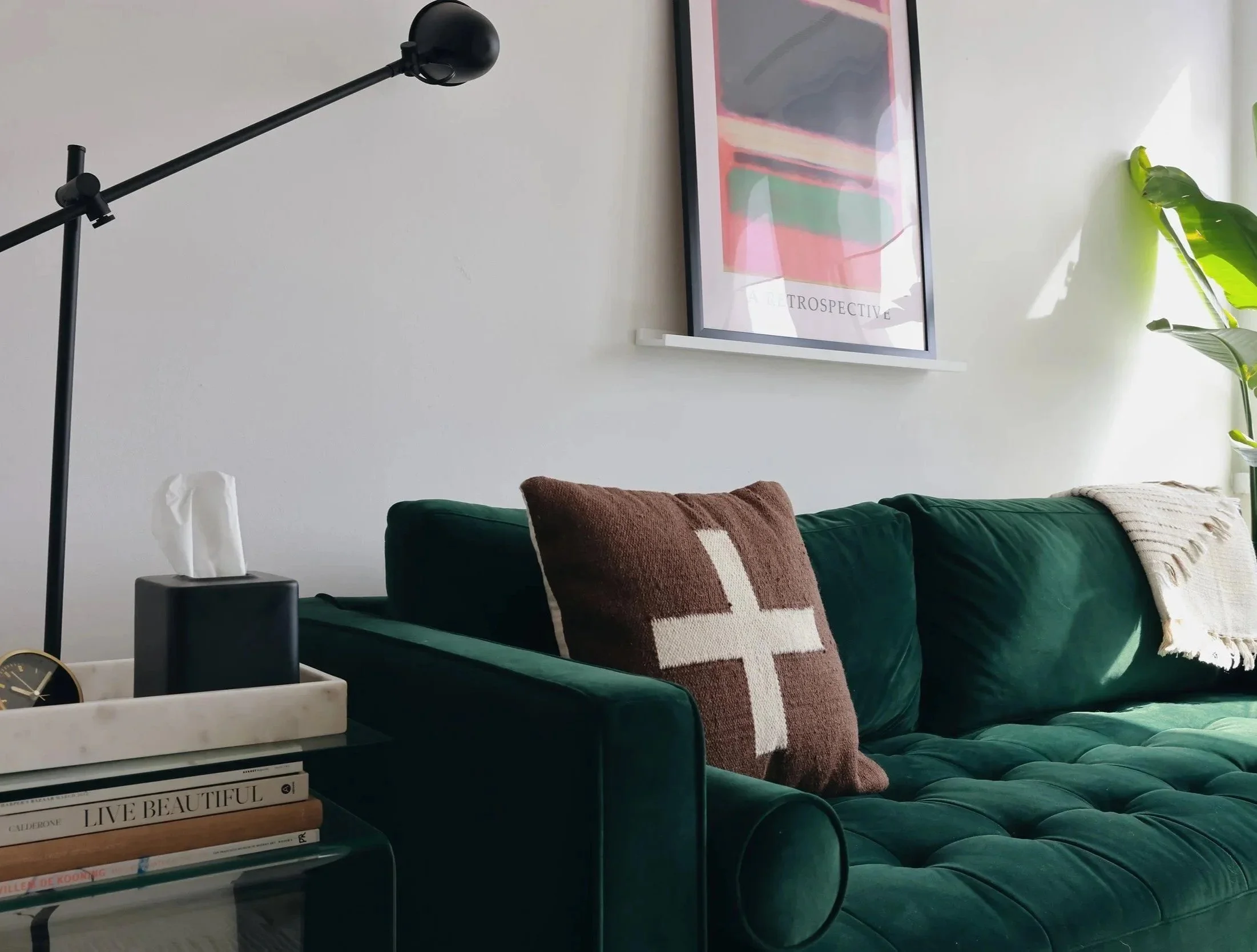 Modern therapy room with a dark green velvet sofa, black floor lamp, abstract wall art, and leafy plant.