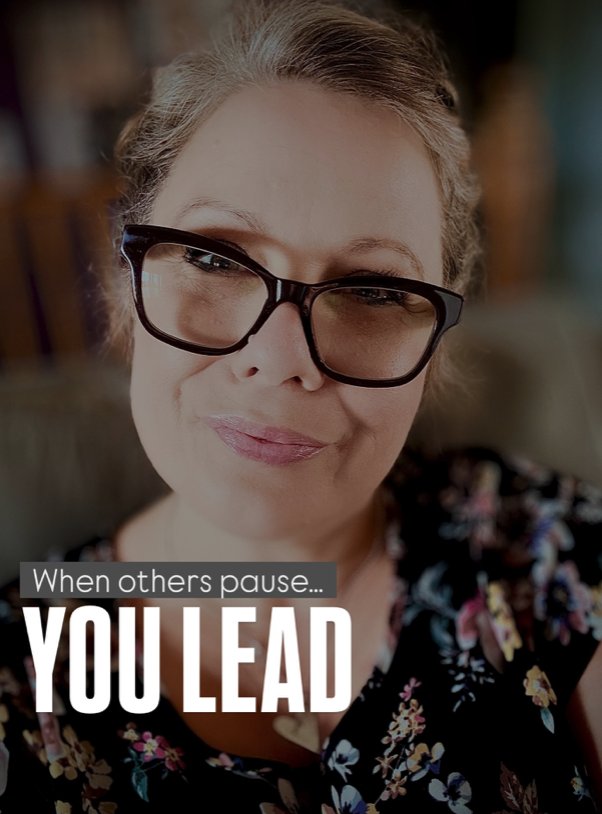 A middle-aged woman with glasses smiling at the camera, wearing a floral top in a cozy indoor setting.