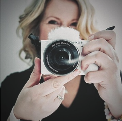 Woman with blonde hair taking a selfie with a white camera wrapped in a fluffy cover.