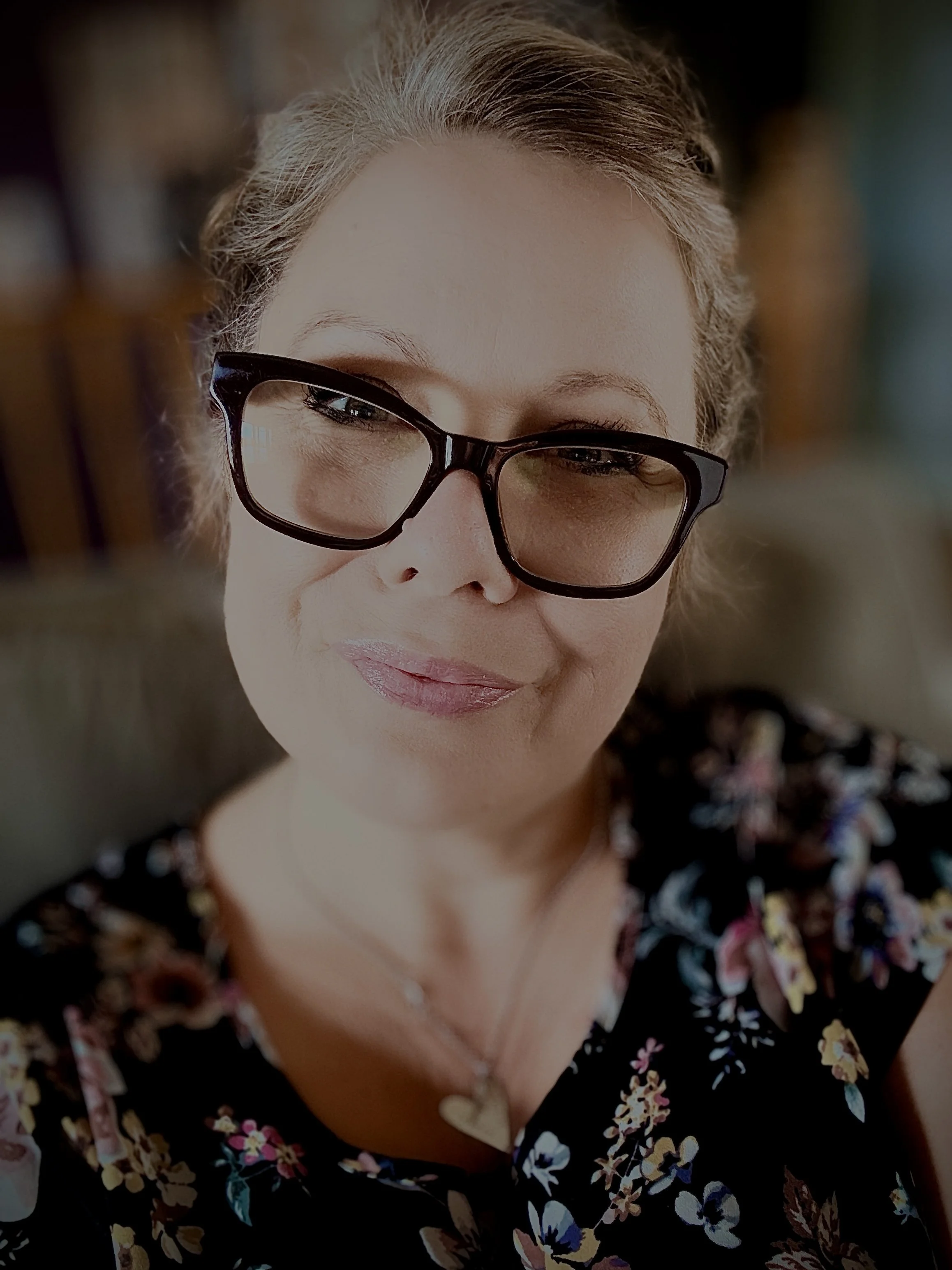 Close-up of a woman wearing black-rimmed glasses and a black floral top, smiling.