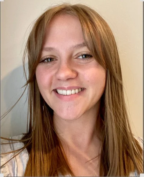 A smiling young woman with long, light brown hair and light skin, posing against a plain background.