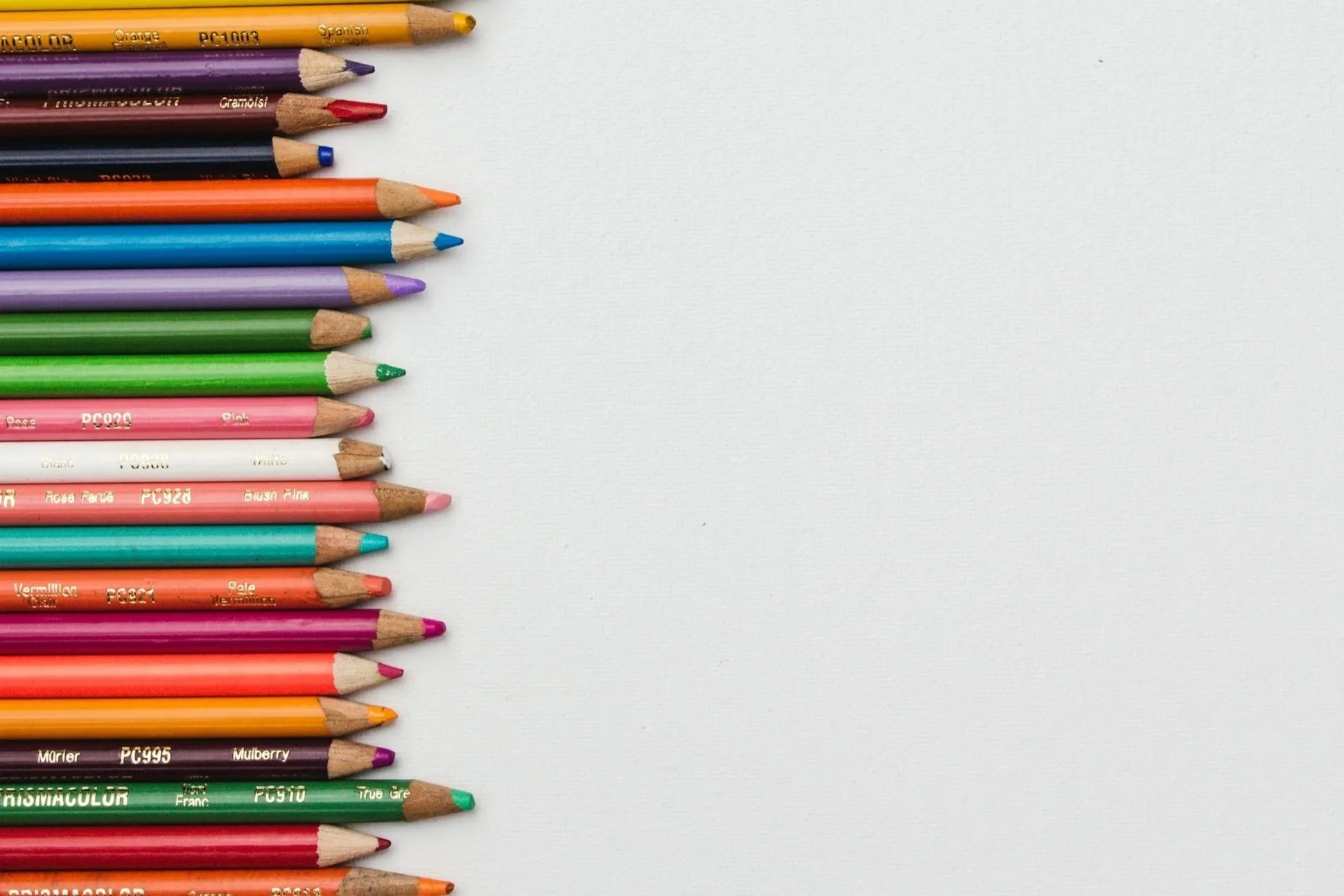 Colorful colored pencils arranged on the left side of a white surface.