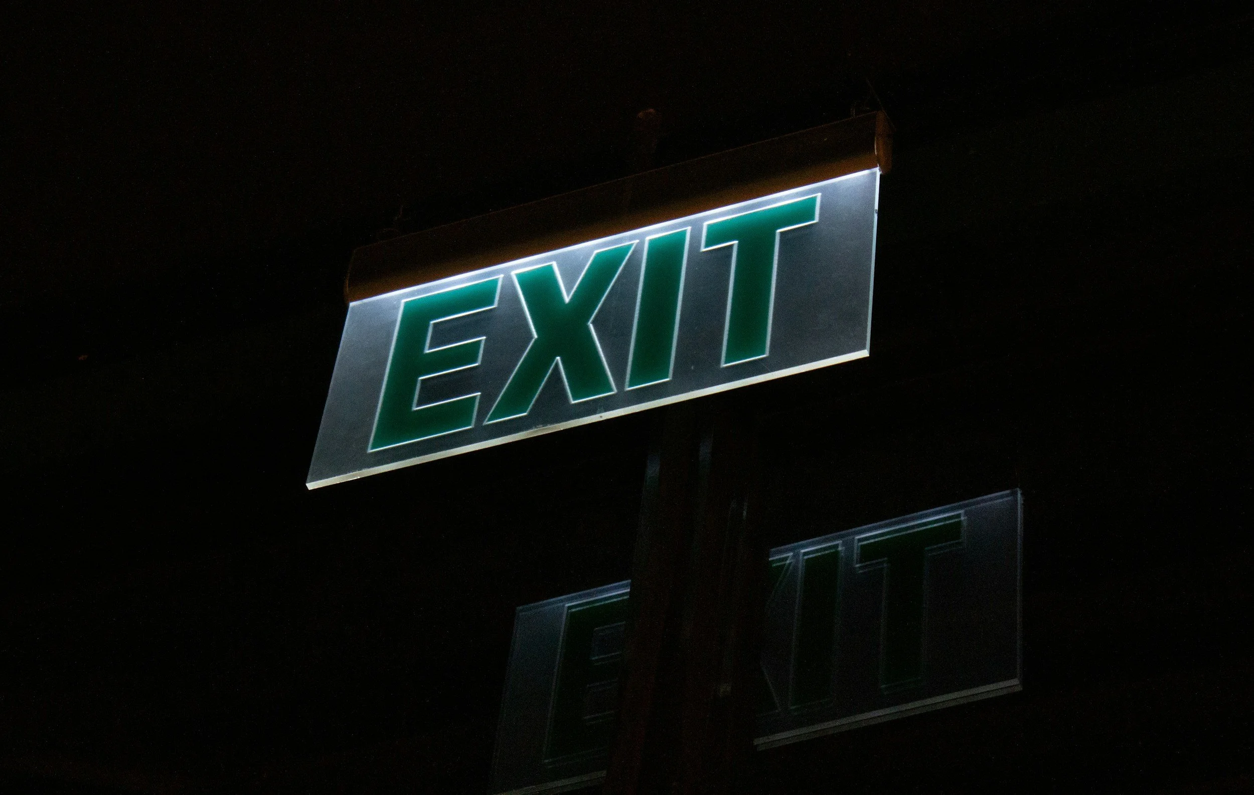 Illuminated green "EXIT" sign at night against a dark background.