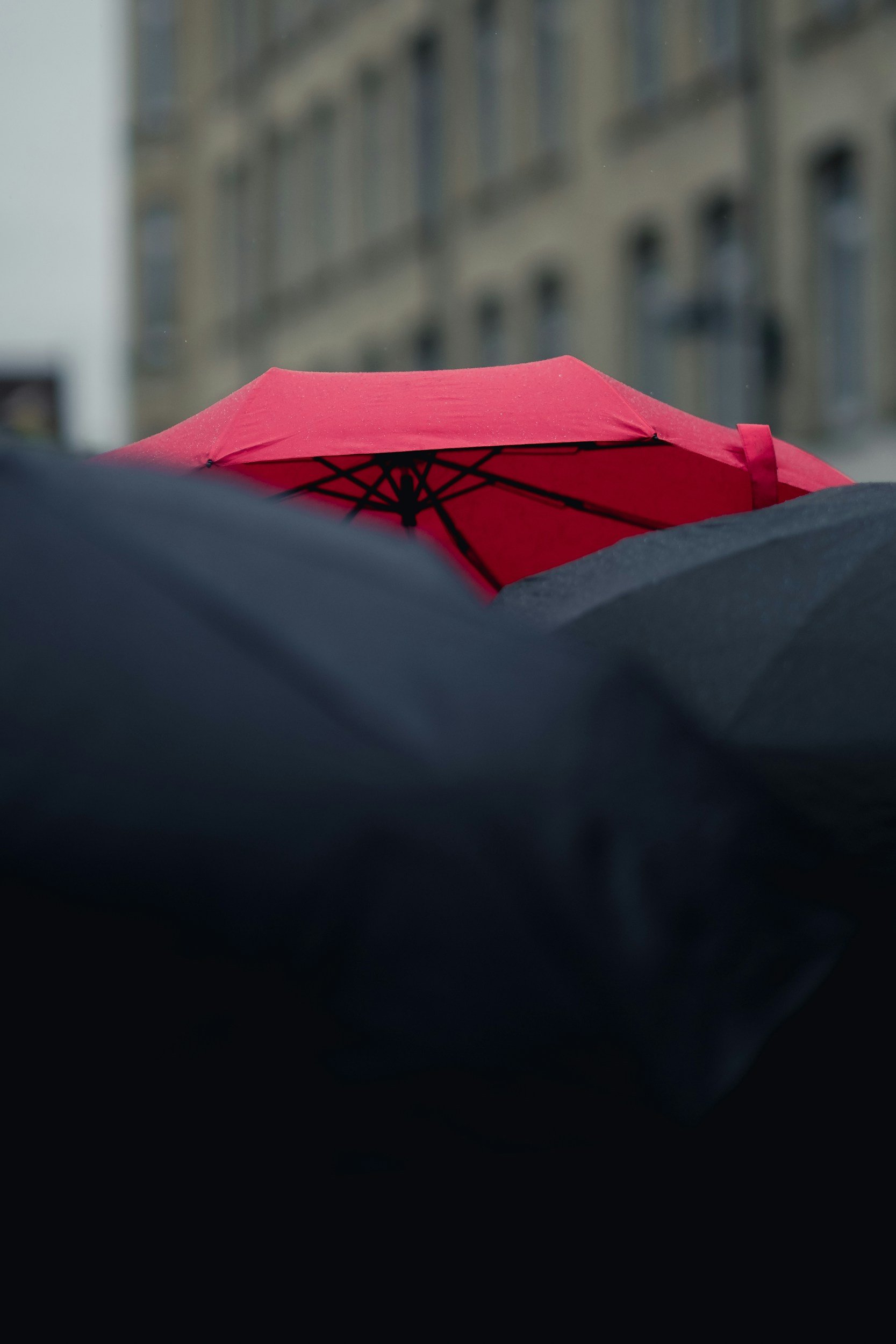 Red umbrella against a blurred urban background with rainy weather.