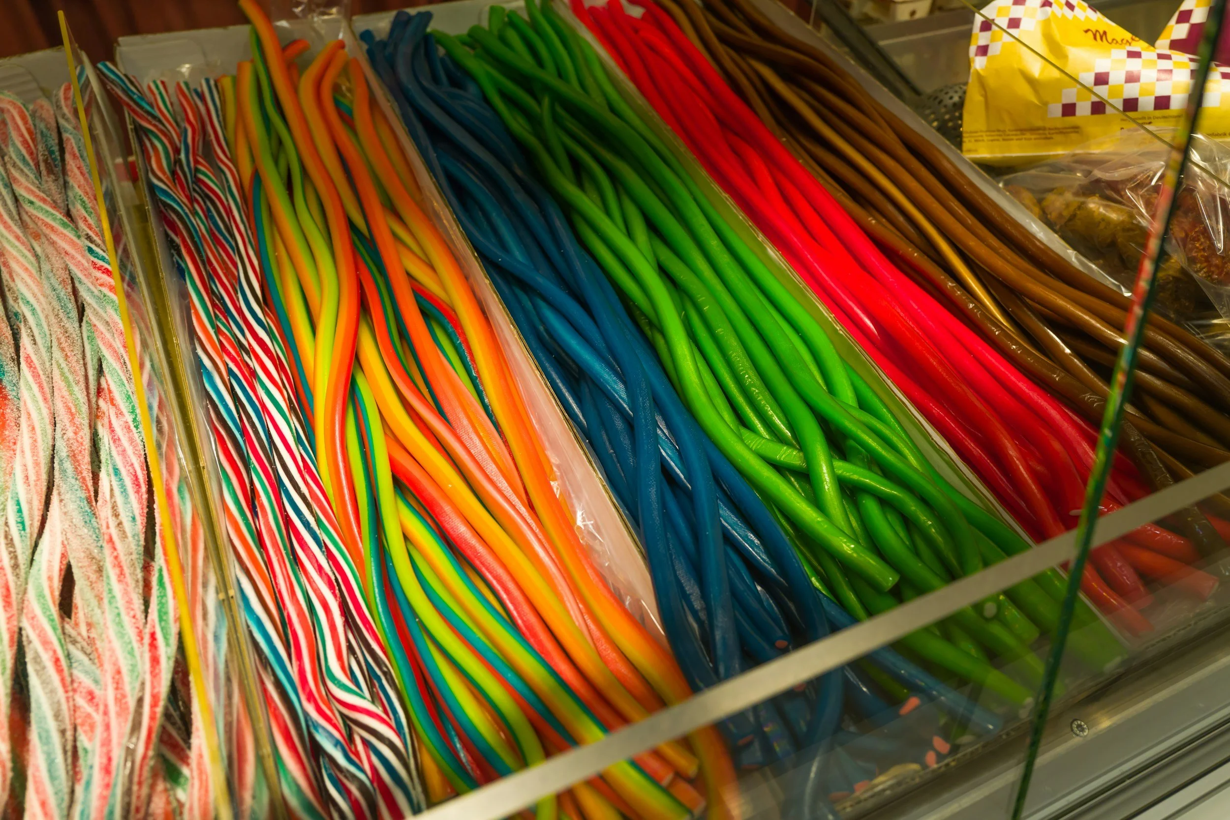 A display of colorful twisted candy canes arranged in rows, including multicolored, blue, green, red, and brown varieties.