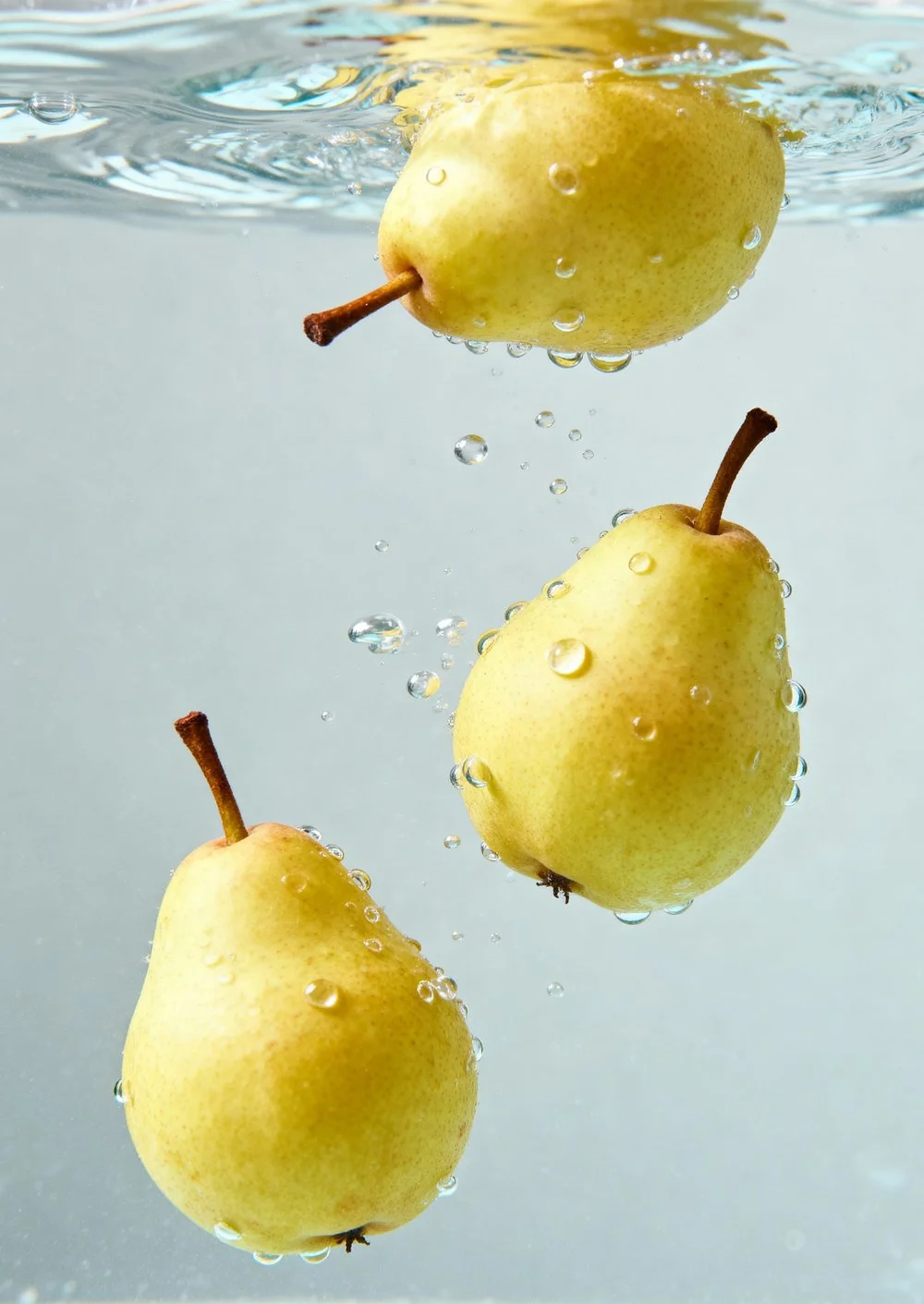 Quatro peras amareladas sendo submersas em água, com bolhas ao redor.