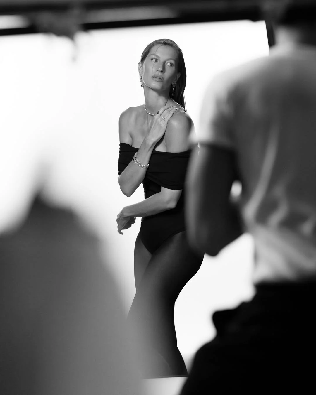 Mulher posando para um ensaio fotográfico em preto e branco, usando joias e um vestido de ombro só, com expressão séria e gestos elegantes.