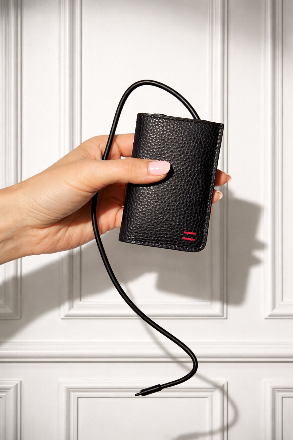Een hand die een zwart, textured portemonnee vasthoudt met een aangehechte USB-kabel, voor een witte paneelachtergrond.