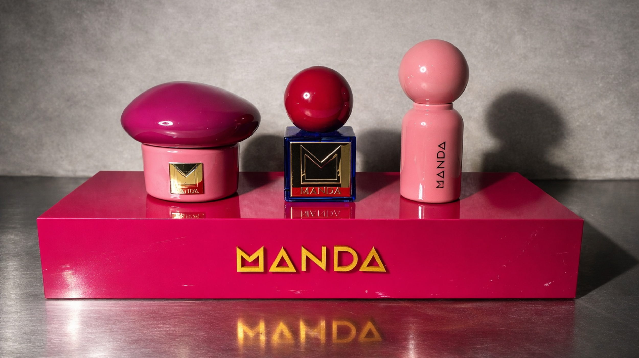Drie kleurrijke parfumflesjes op een roze platform met de naam 'MANDA' in goud.