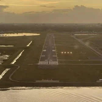 View of an airport runway at sunset with lights and surrounding flat landscape.