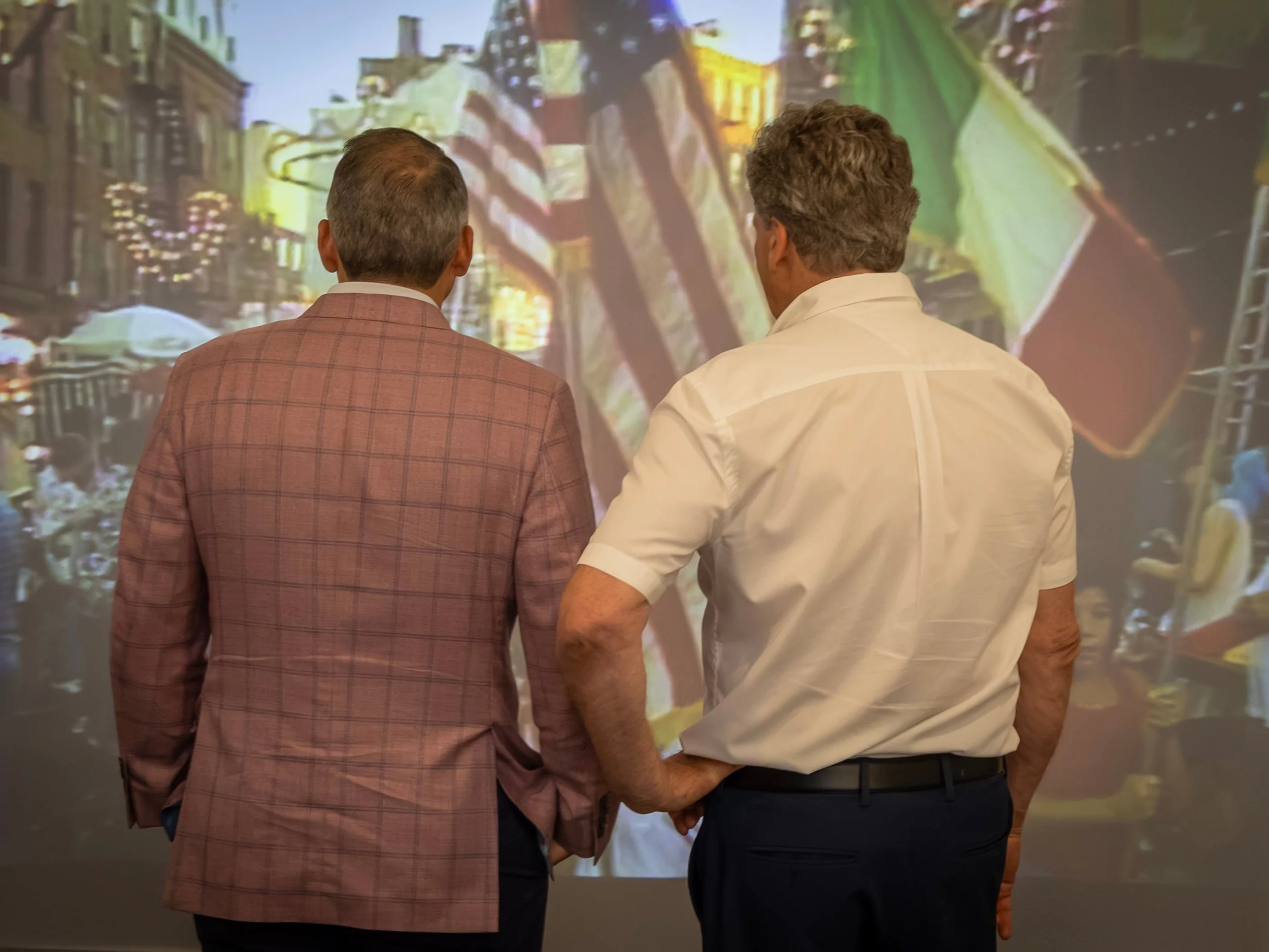 Summer feast footage with American and Italian flags on the museum's projection wall.