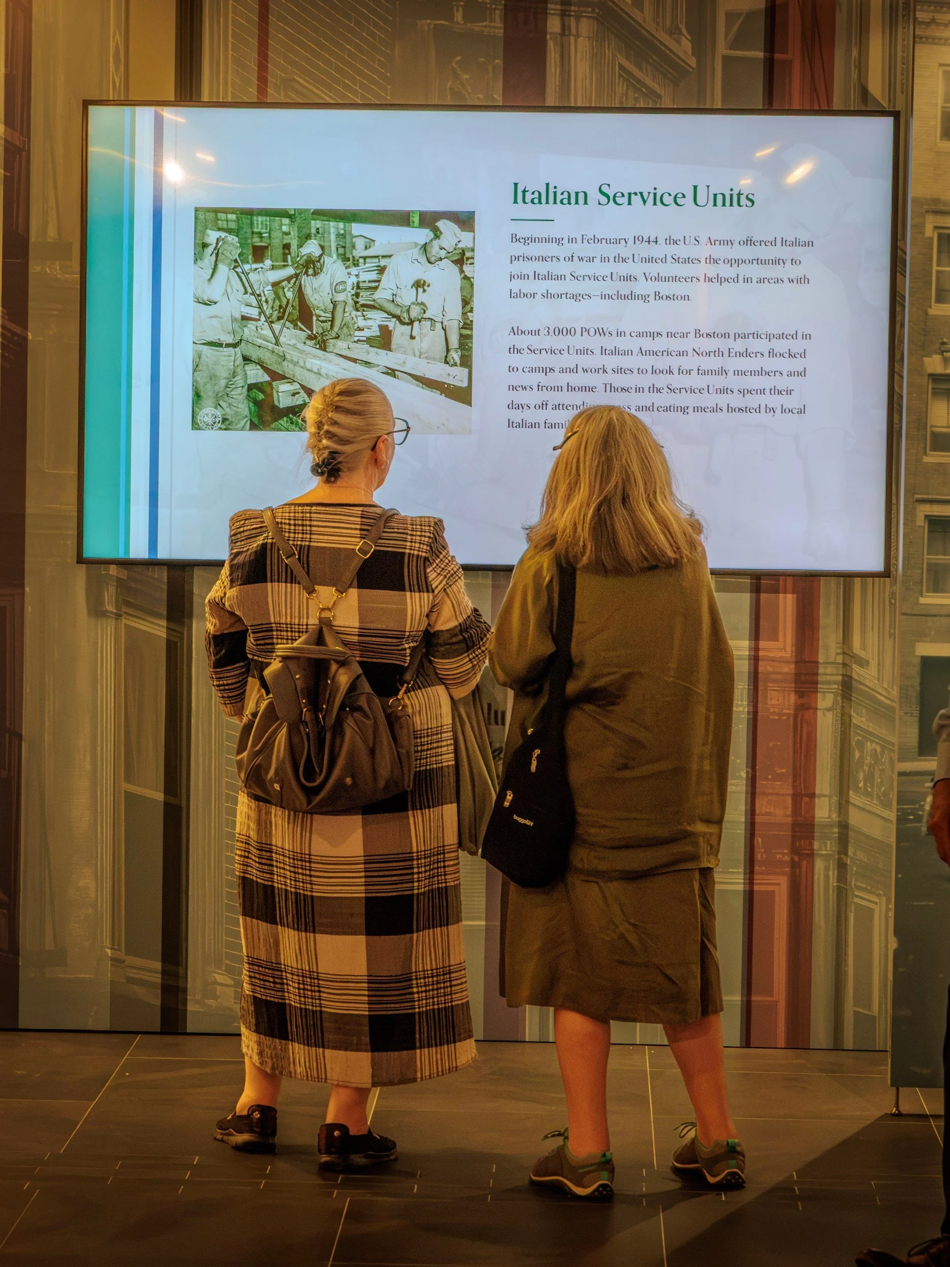 Two visitors reading the Italian Service Units panel about Italian prisoners of war hosted by North End families in 1944.