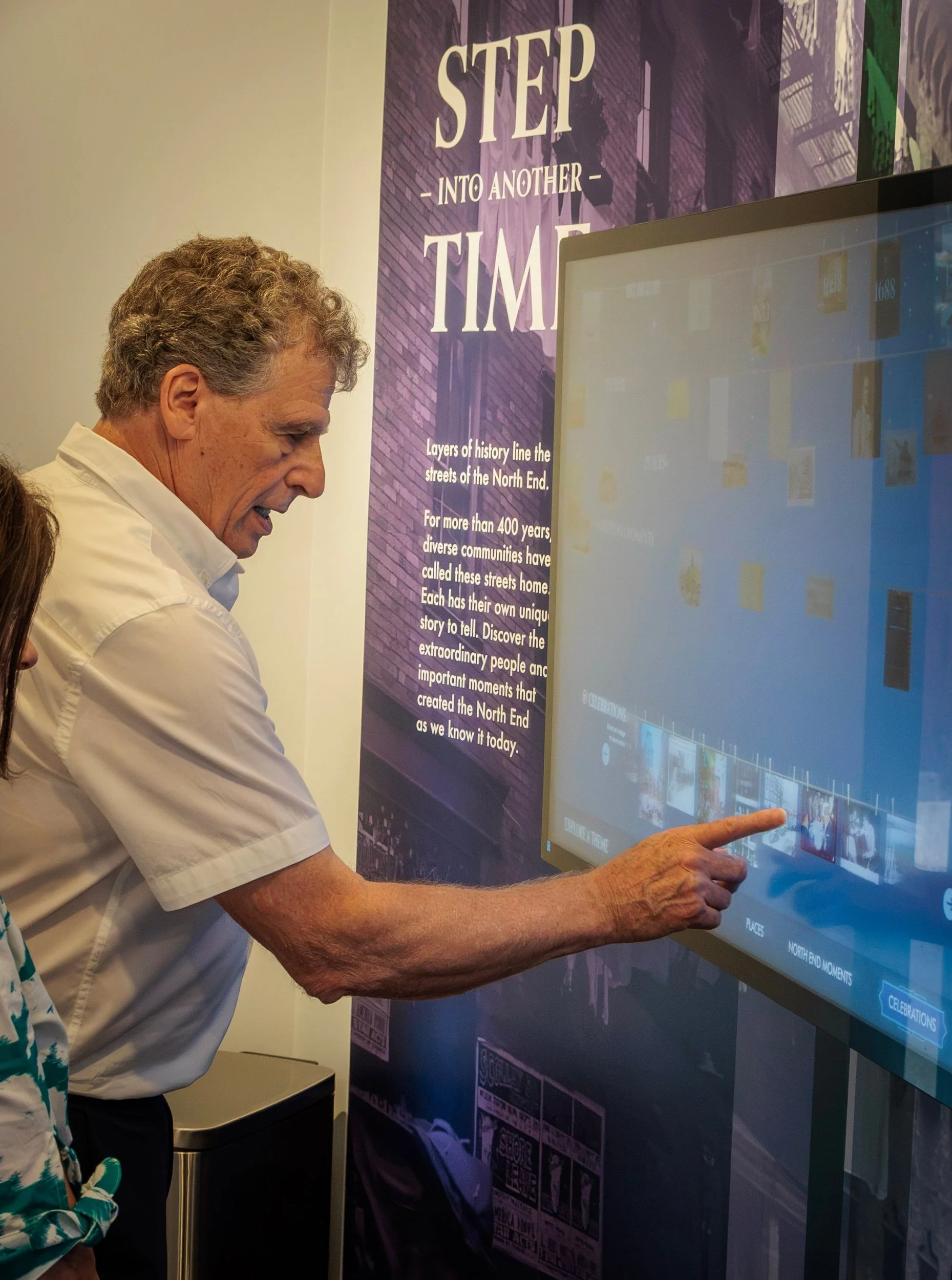 A visitor uses the Step Into Another Time touchscreen at the North End Historical Museum, the introduction that opens the visit.