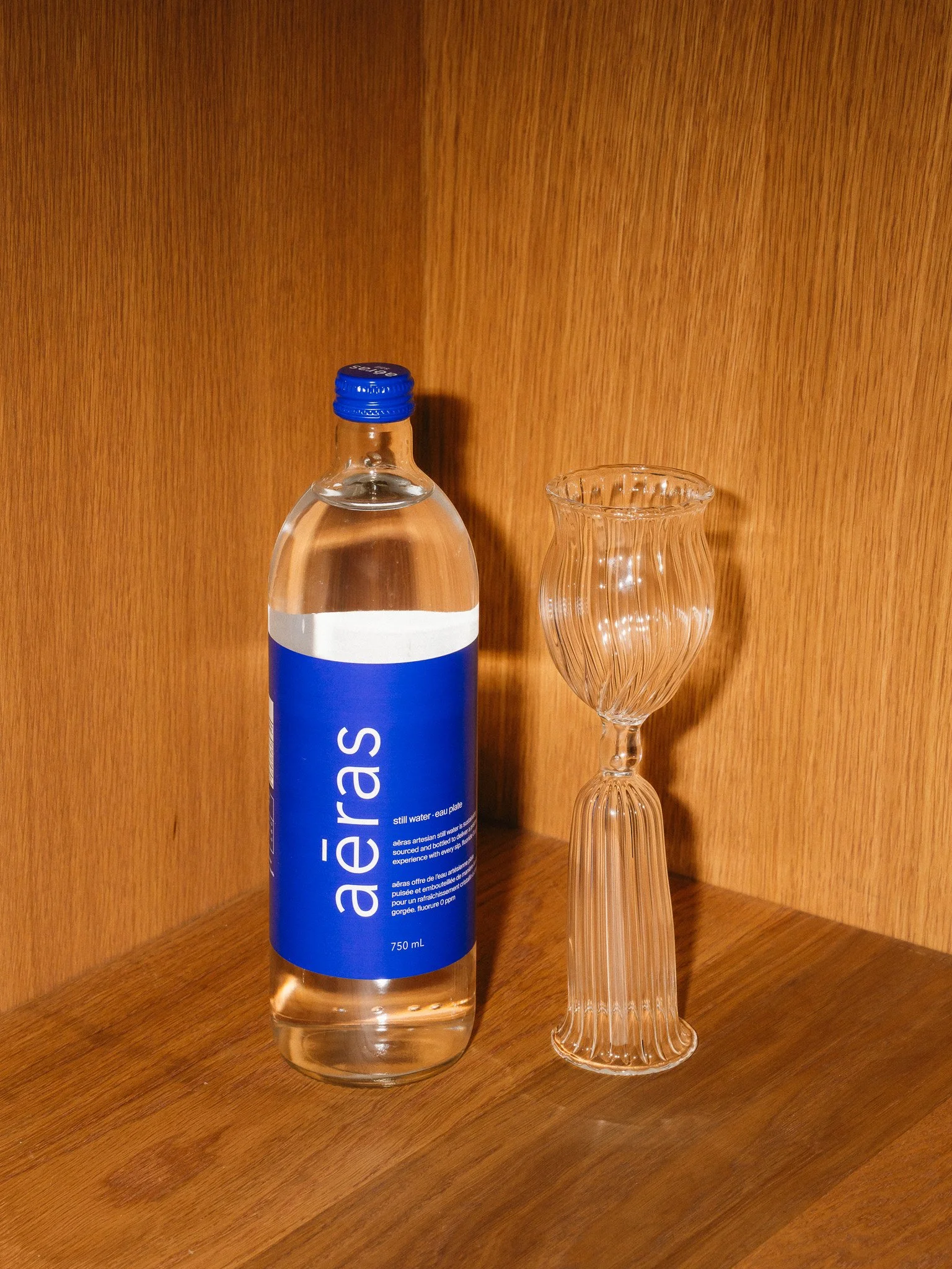 A bottle of still water labeled 'aéreas' and an empty decorative glass on a wooden surface in a wood-paneled room.