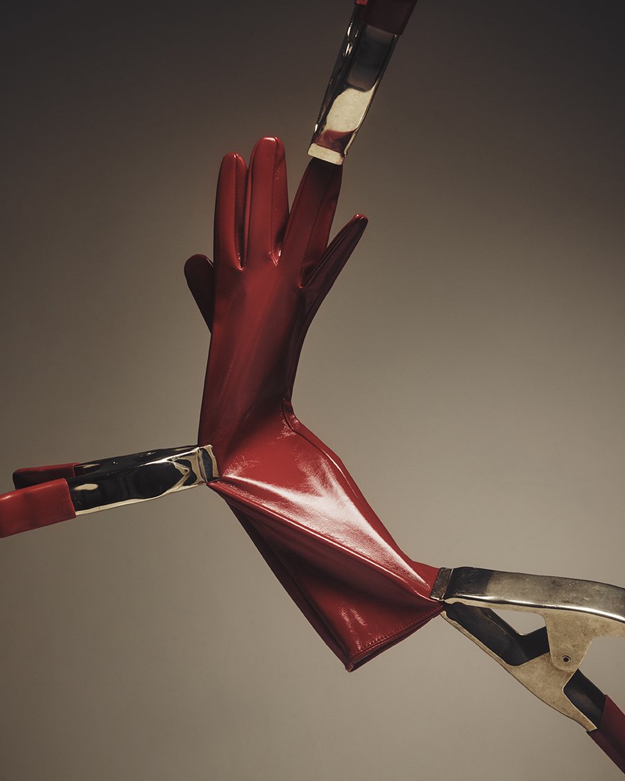 A red rubber glove being held up by two metal tongs against a dark background.