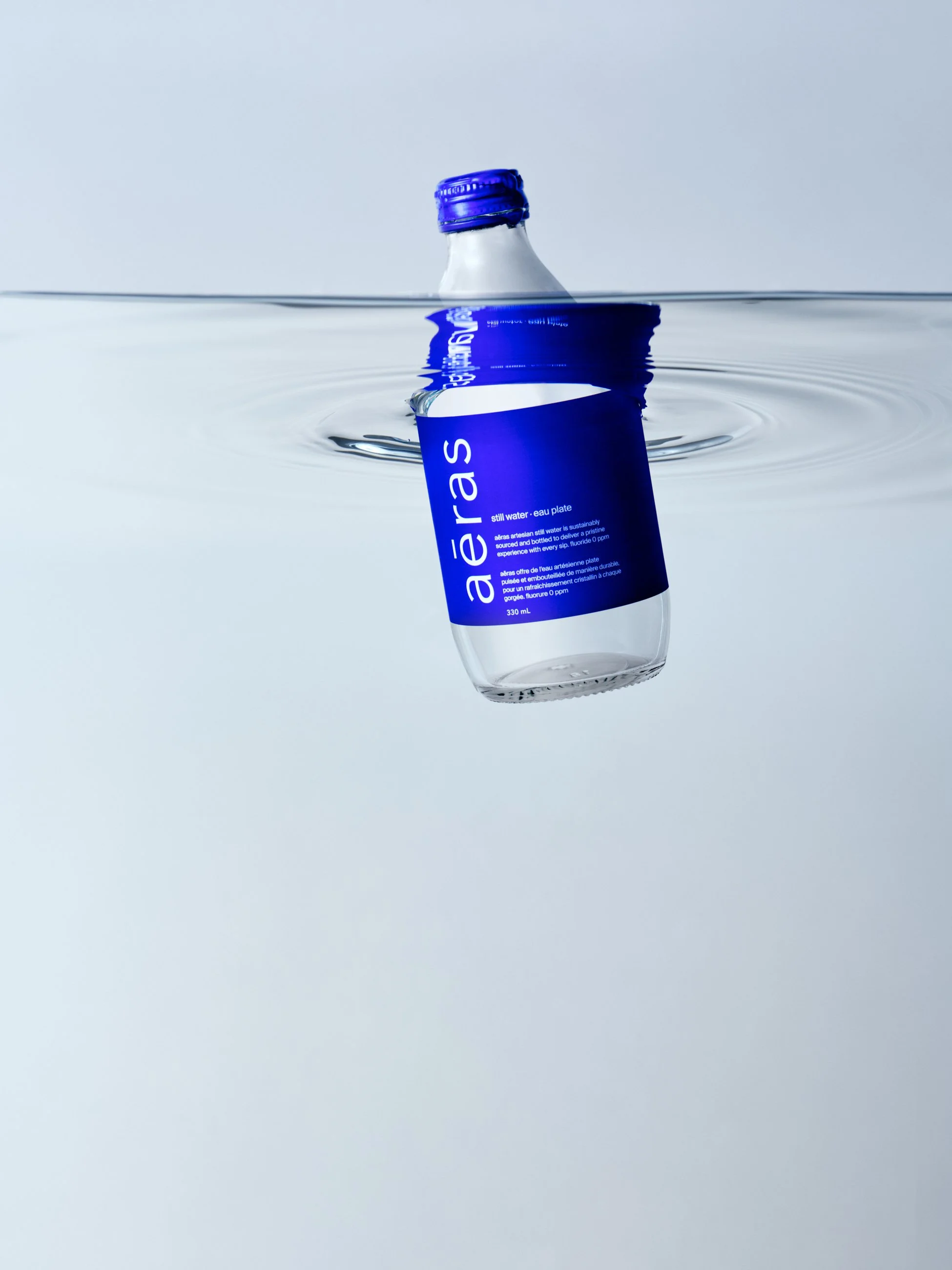 A plastic water bottle labeled 'aeras' is floating upside down in water, with half of the bottle submerged.