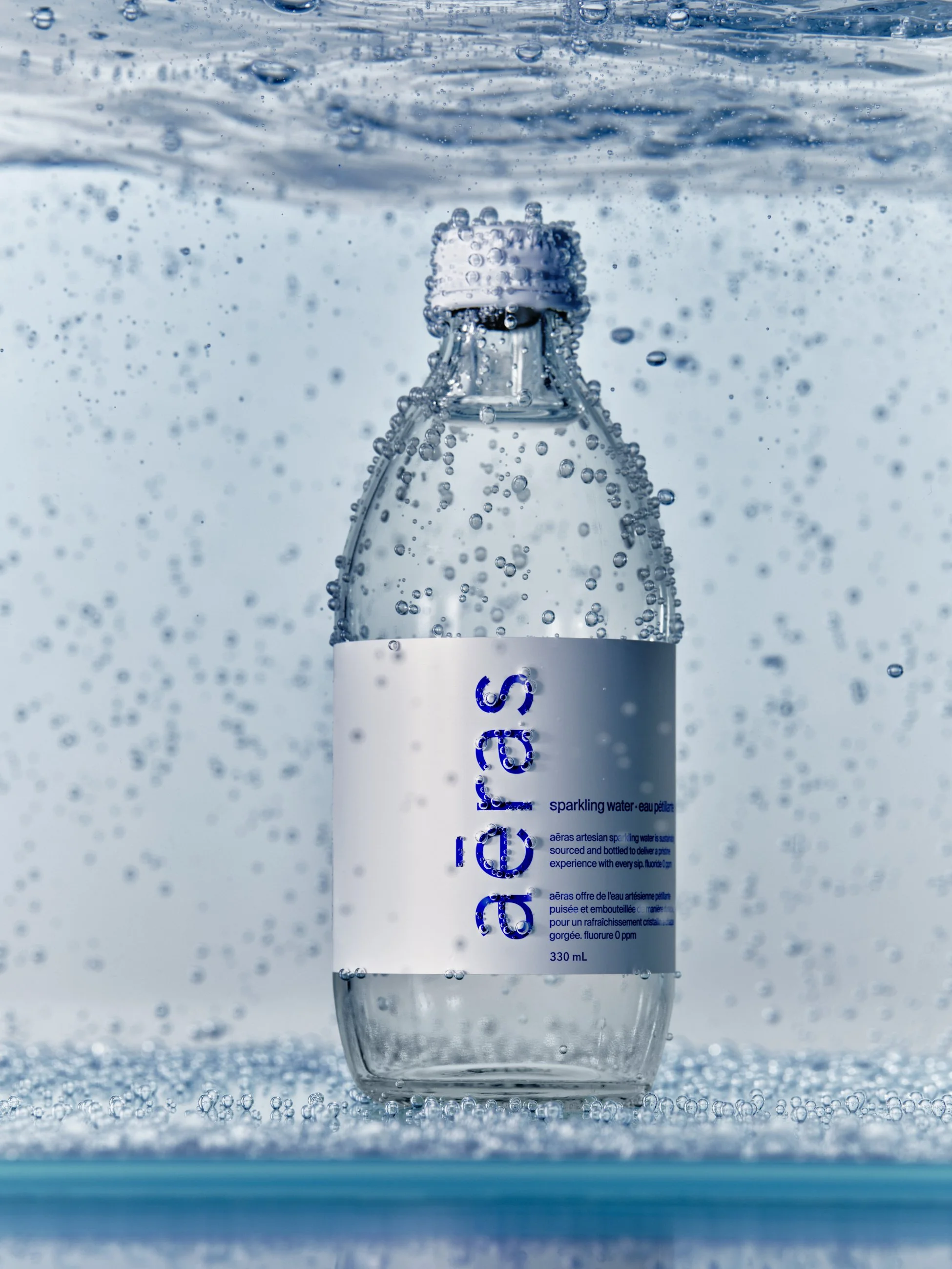 A clear plastic bottle of sparkling water labeled 'aeres' submerged in water with bubbles around it.