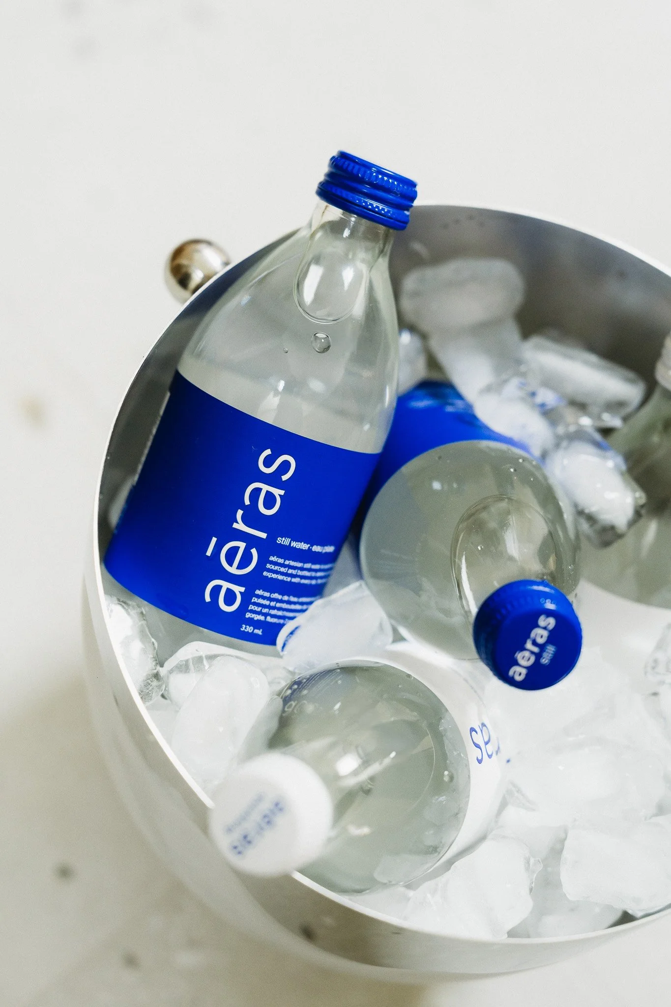 Several bottles of Aeras still water in a metal ice bucket with ice cubes.
