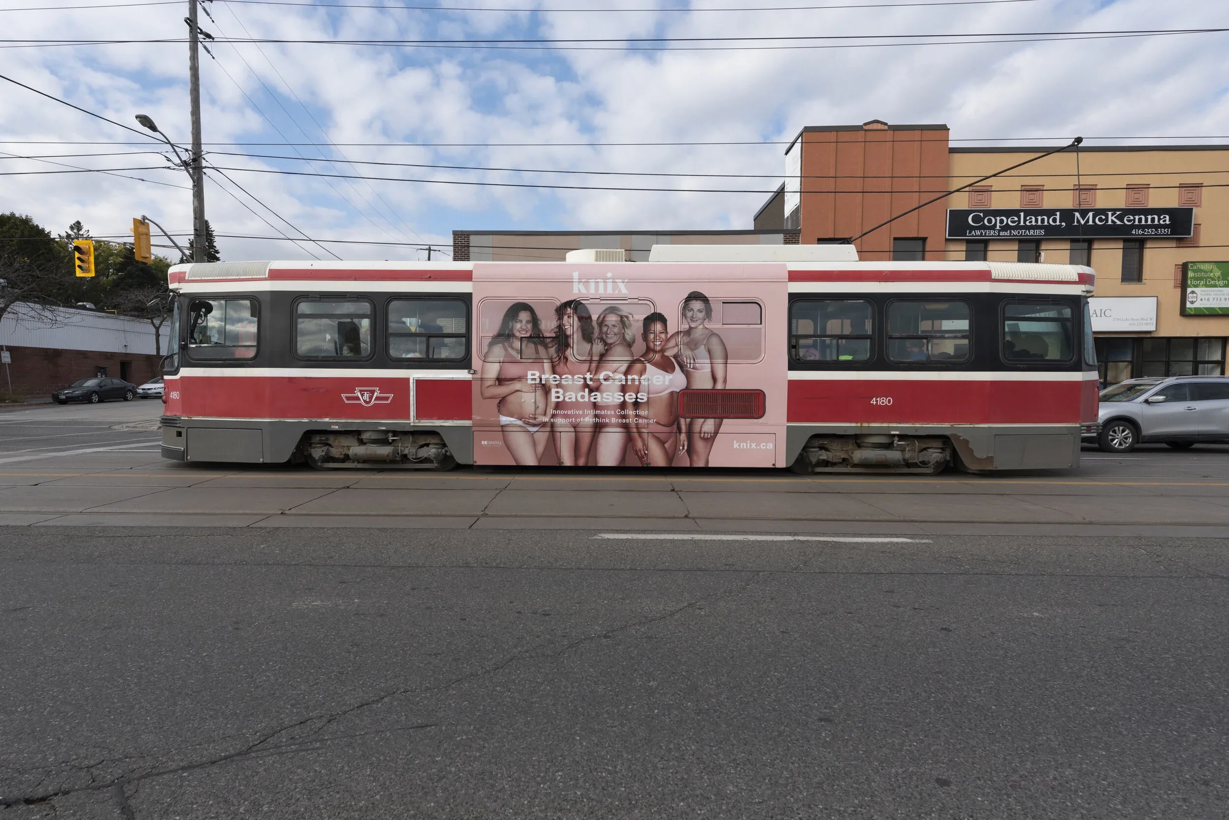 A streetcar with a pink advertisement showing four women in lingerie promoting breast cancer awareness, with the text 'knix Breast Cancer Badasses' and the website 'knix.ca'.