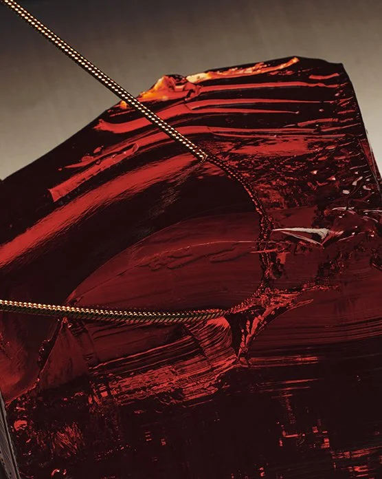 Close-up of a shattered red glass object with a silver chain or wire draped over it.