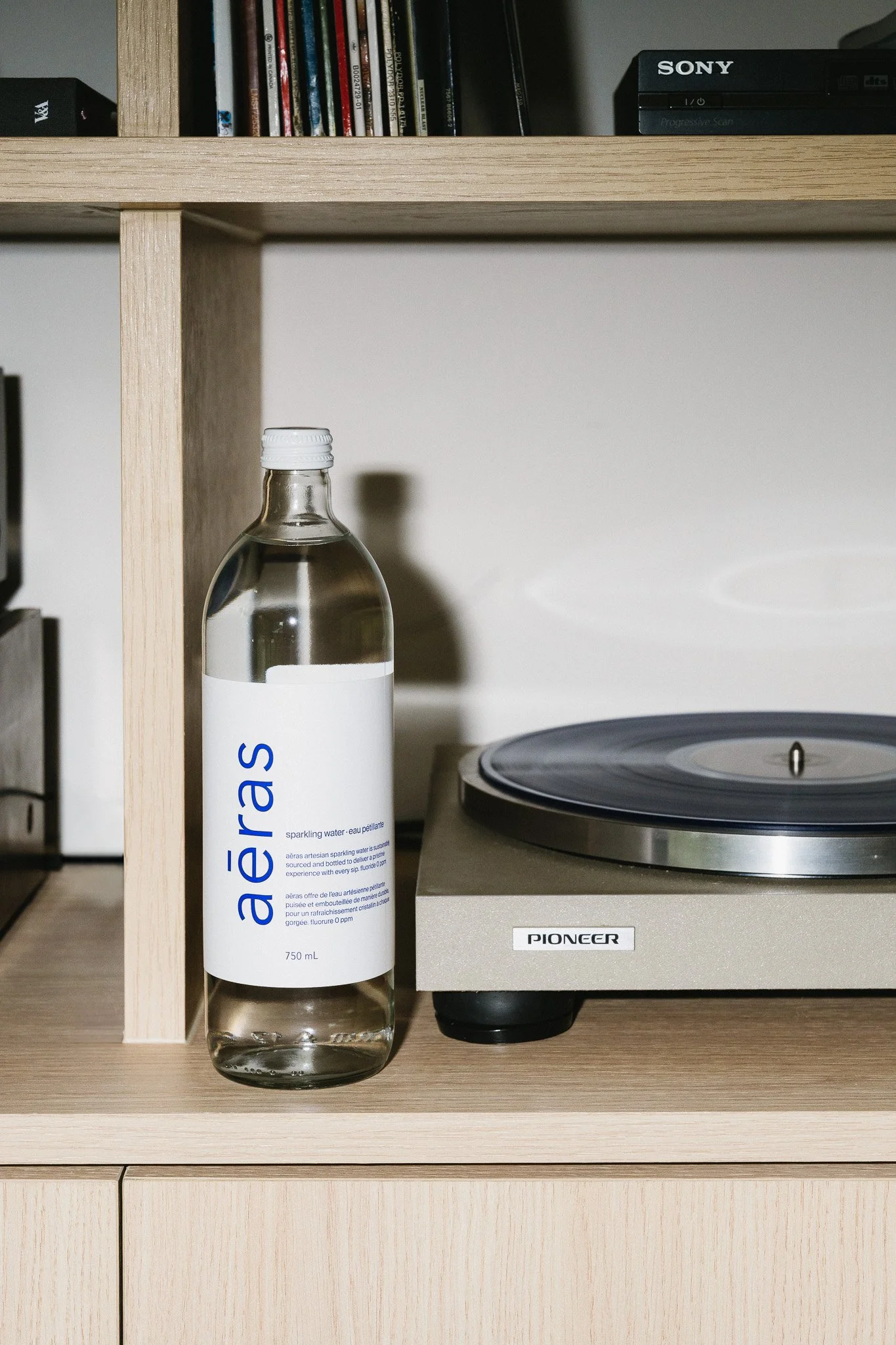 A bottle of sparkling water labeled 'aèrās' next to a turntable on a wooden shelf.
