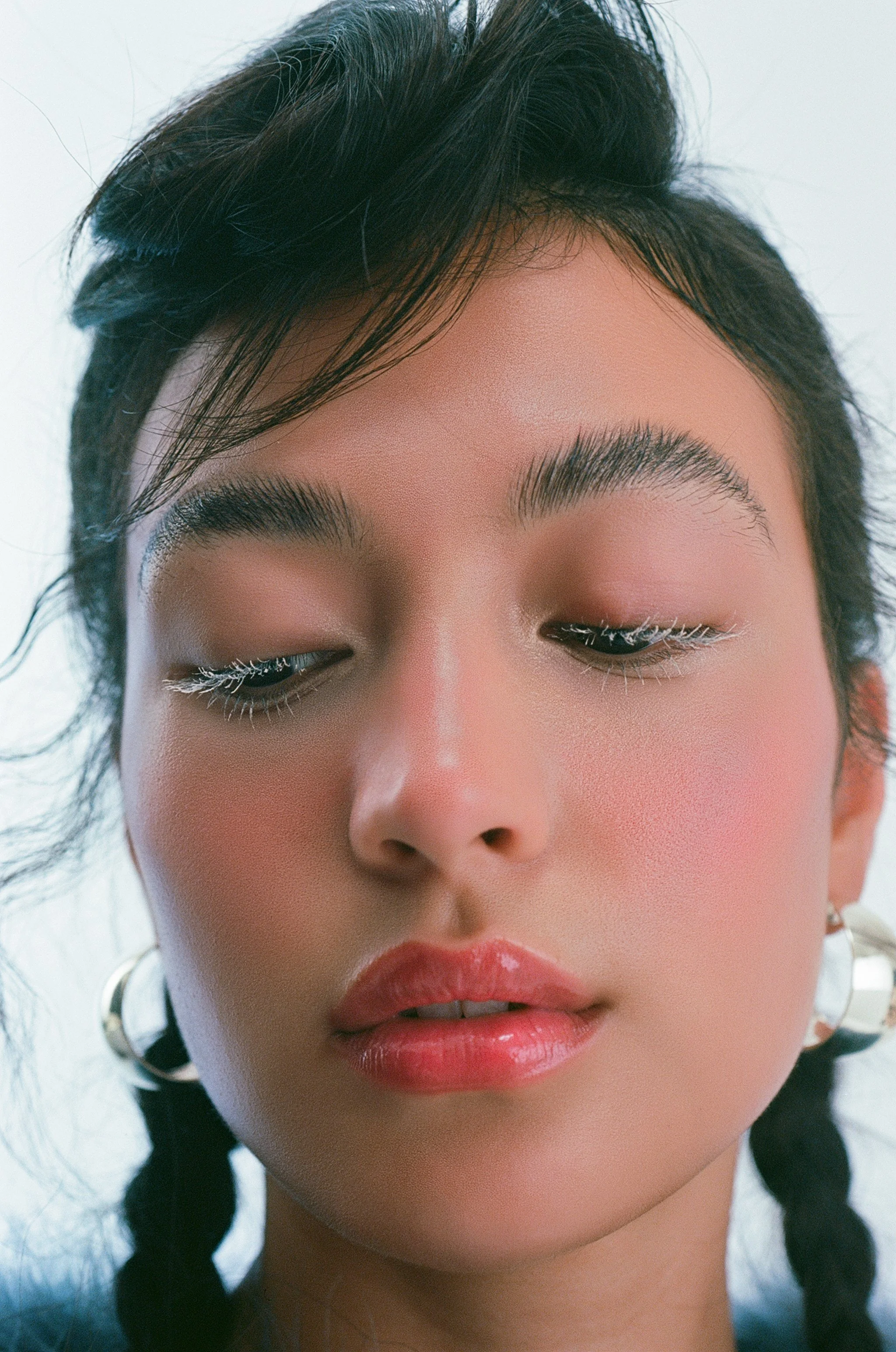 Close-up of a young woman with makeup, wearing hoop earrings, with her eyes closed.