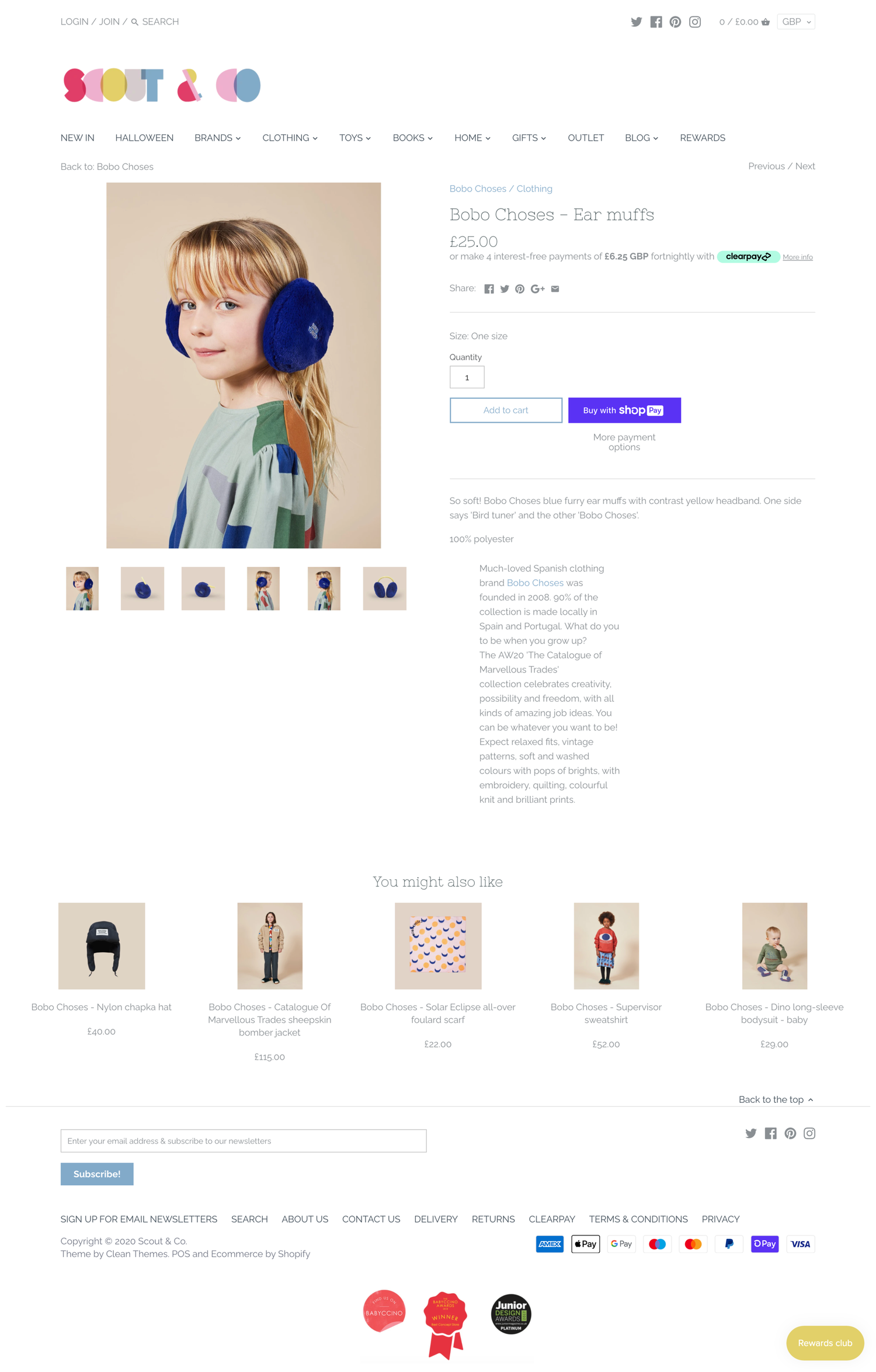 A young girl with blonde hair wearing blue furry ear muffs and a colorful dress, posing against a beige background.